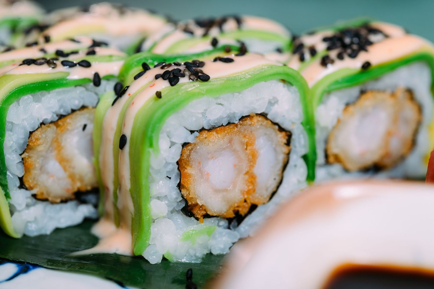 Close-up view of fresh sushi rolls with green garnish and black sesame seeds arranged on a dark surface.