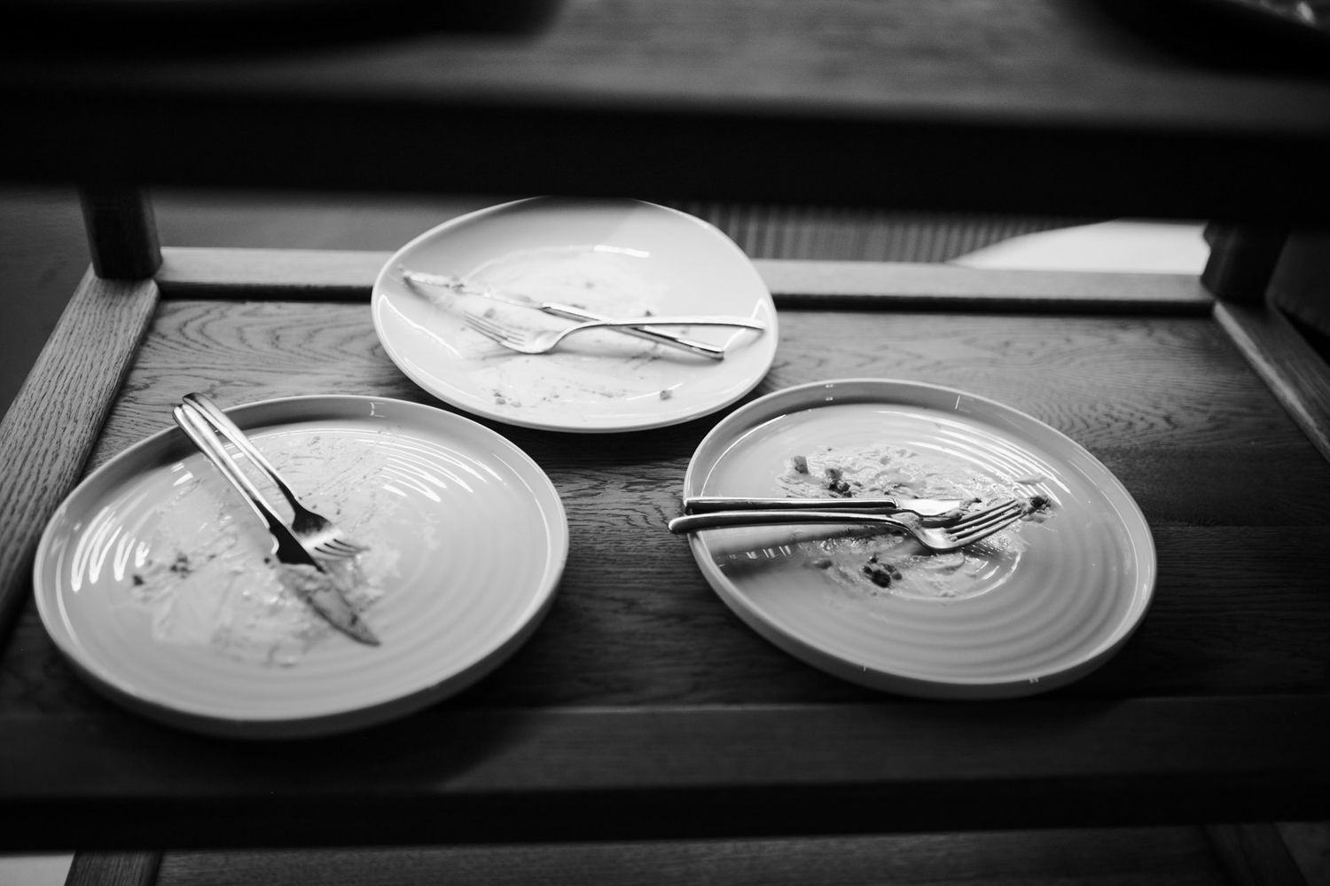 Black and white image of empty dinner plates arranged on a dark surface.