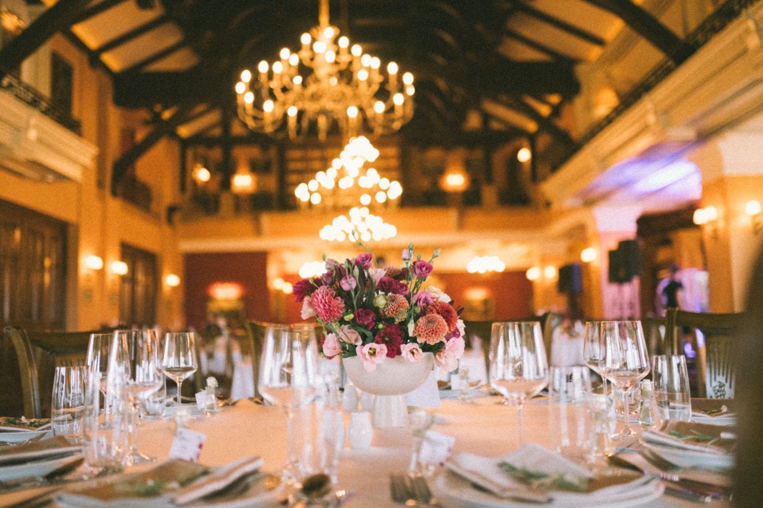 Elegant wedding reception venue with crystal chandeliers and warm lighting illuminating multiple decorated dining tables.