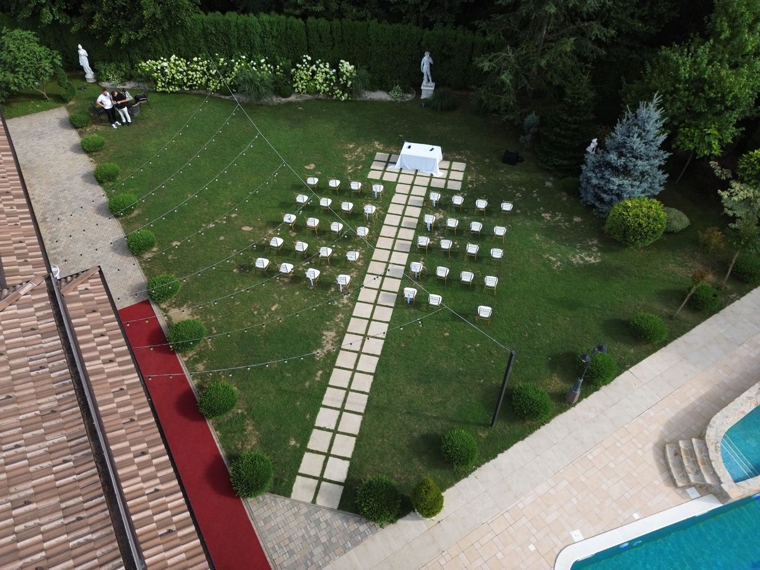 Aerial view of an outdoor wedding ceremony setup with white chairs arranged in rows near a pool.
