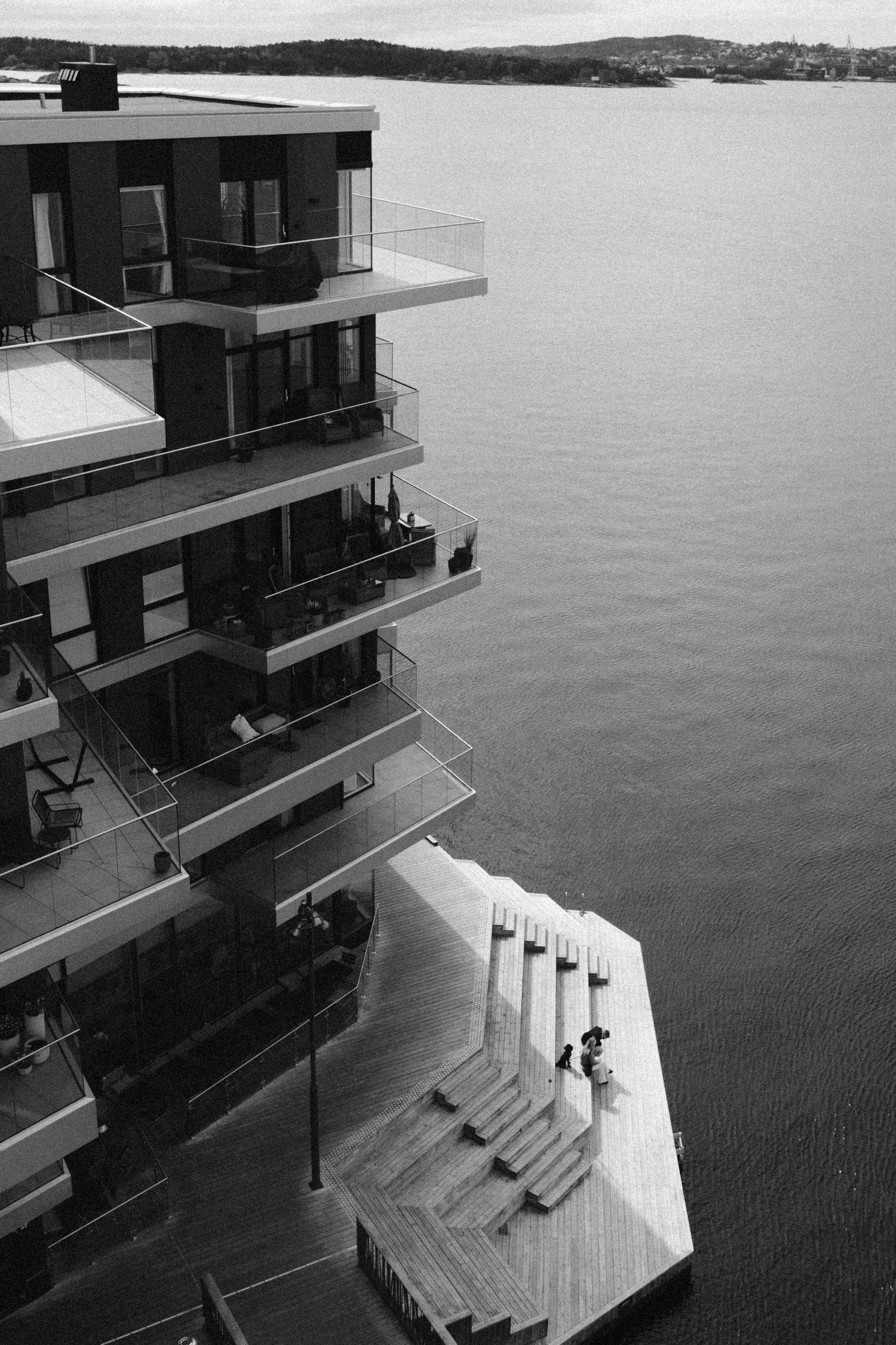 Modern apartment building with cascading balconies overlooking a calm waterfront in black and white photography.