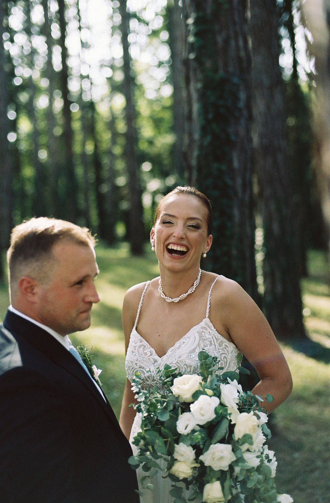 Candid wedding moment in a forest setting with white roses and greenery bouquet.