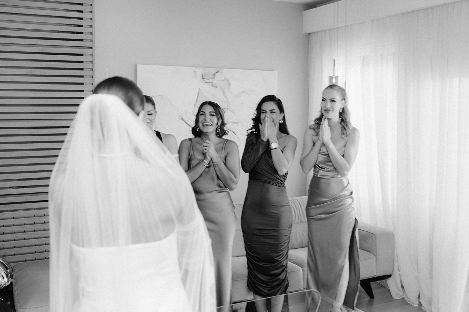 A series of black and white photos showing wedding preparation moments with people getting ready in a bright room.