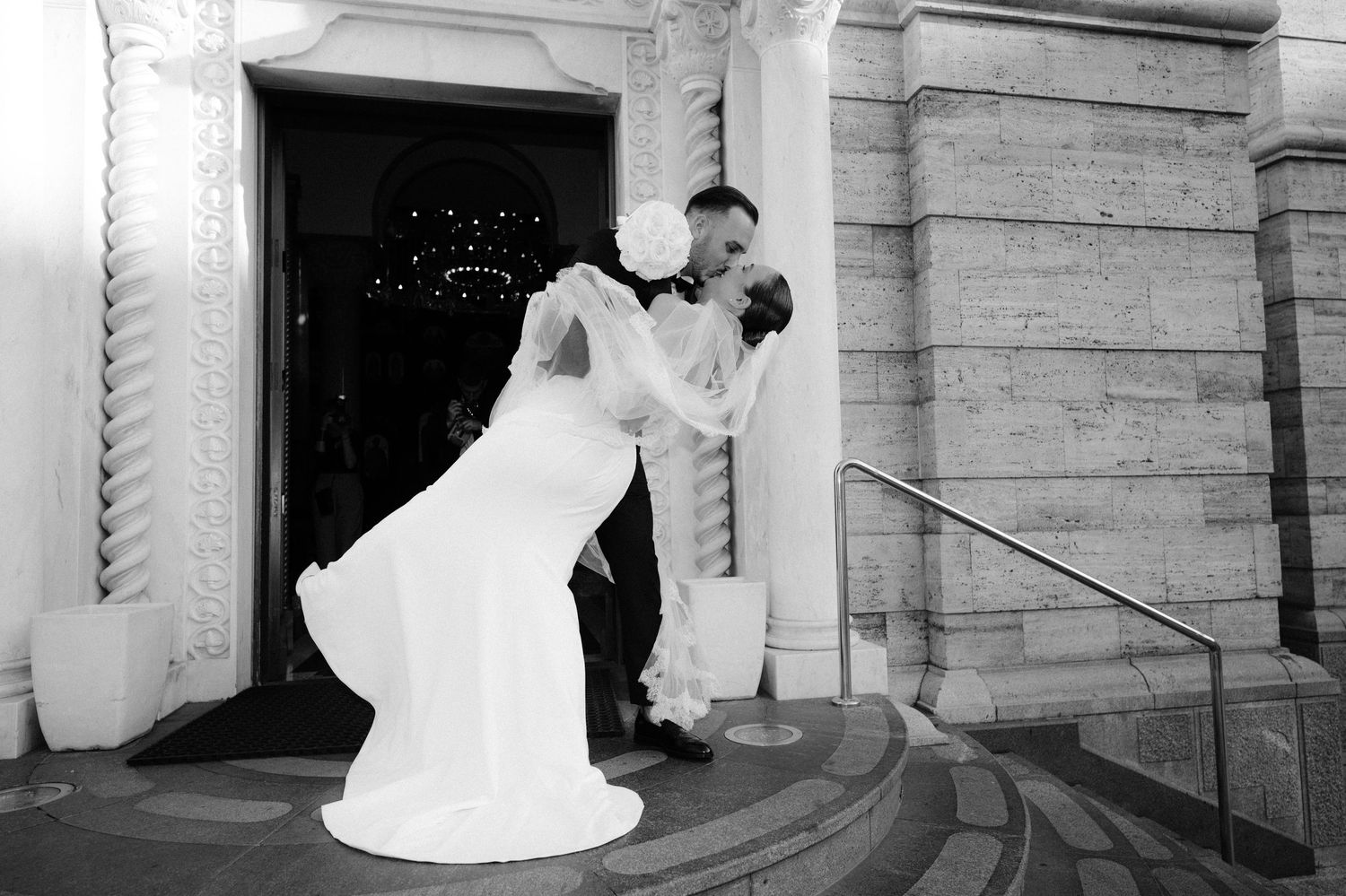 A series of black and white wedding photos showing romantic moments between newlyweds in front of stone architecture.
