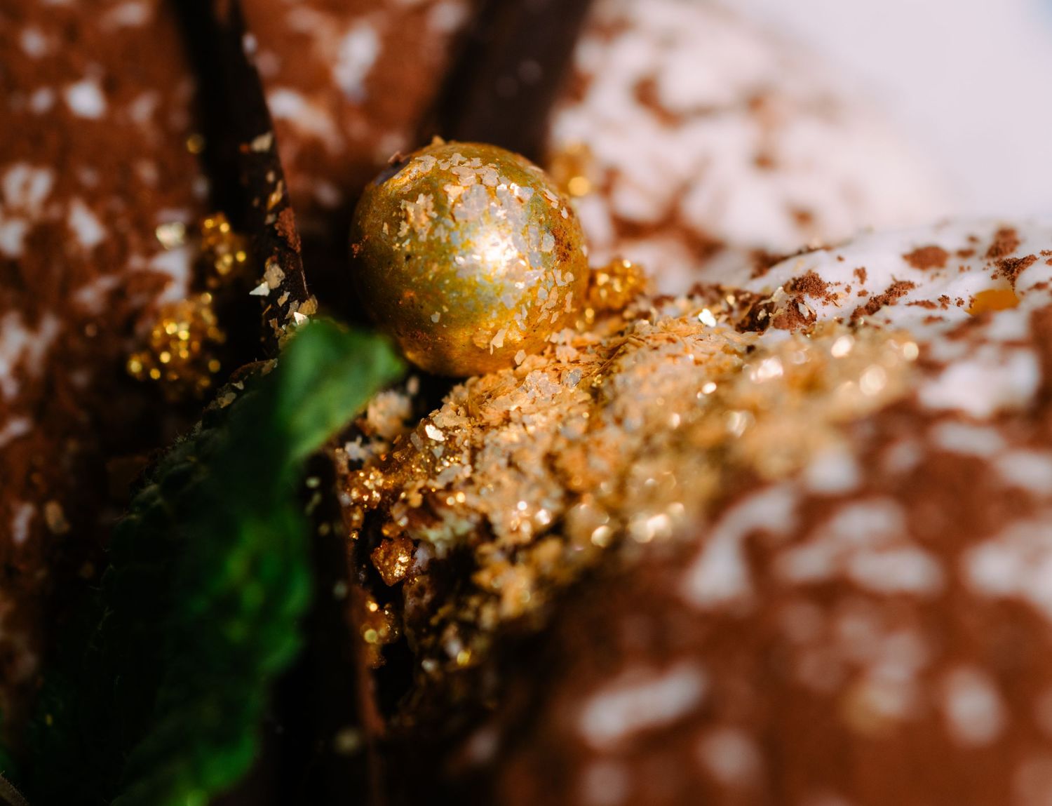 A close-up macro shot shows golden glitter and chocolate textures in an artistic abstract composition.
