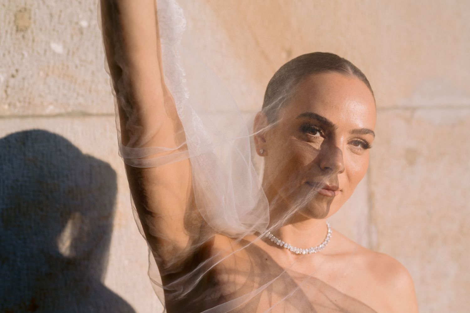 Artistic portrait through sheer fabric with dramatic shadows against a beige wall.