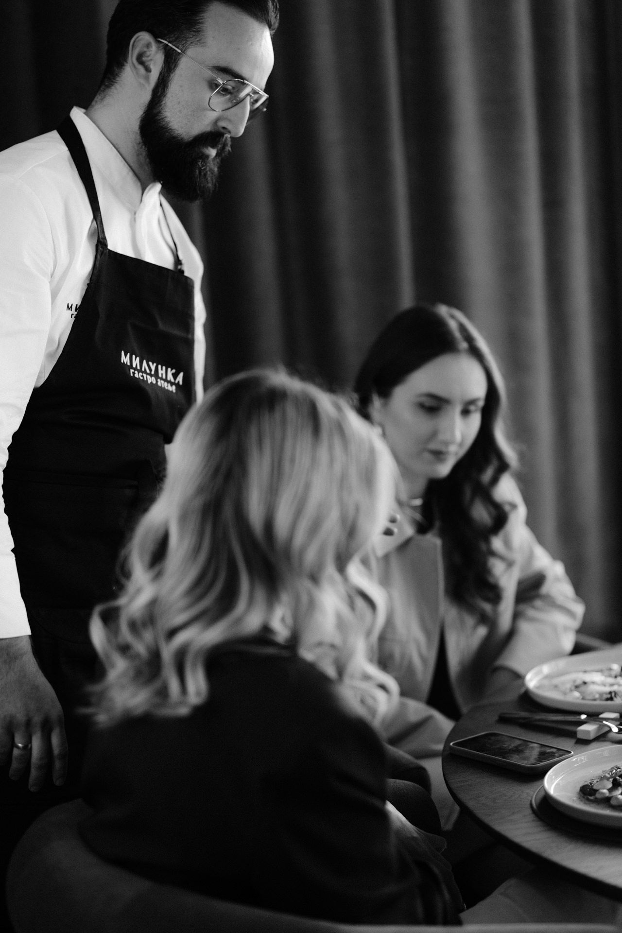 Chefs in black aprons prepare elegant dishes at a fine dining restaurant.
