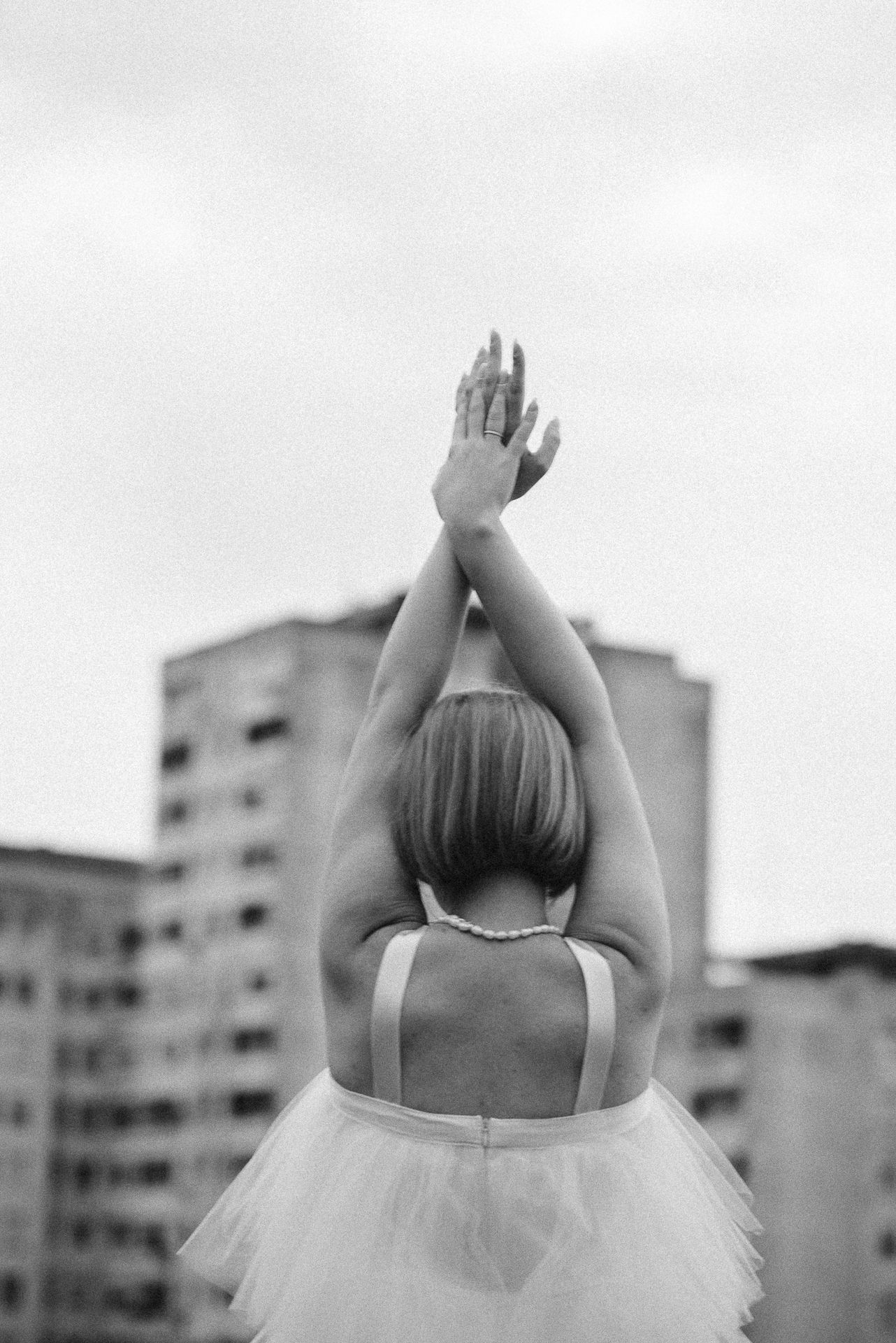 Crno-bijela fotografija mlade u haljini dok graciozno podiže ruke prema gradskim zgradama u pozadini Banja Luka.