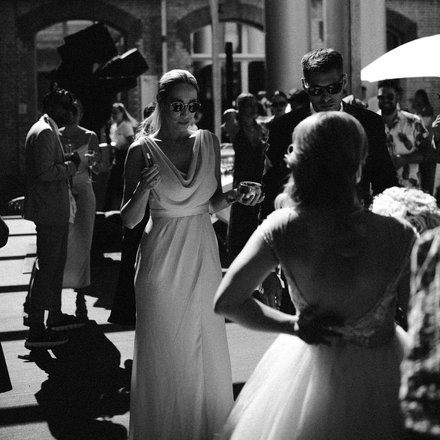 Crno-bijela fotografija elegantnih žena u bijelim haljinama na ceremoniji vjenčanja na otvorenom.