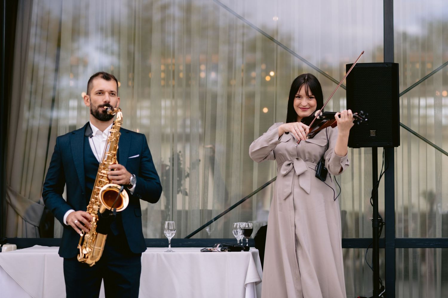 A man in a suit plays saxophone while a woman in gray plays violin at an elegant indoor event.