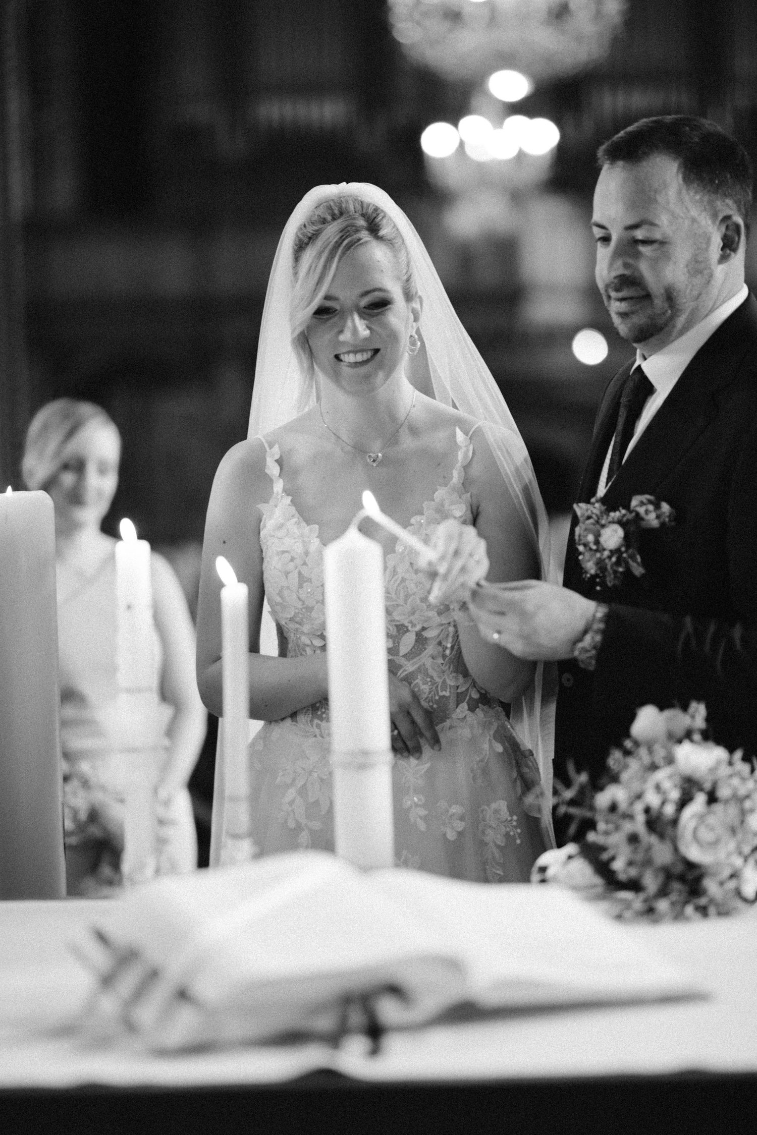 Black and white photo of a smiling bride and groom lighting candles during a church wedding ceremony.