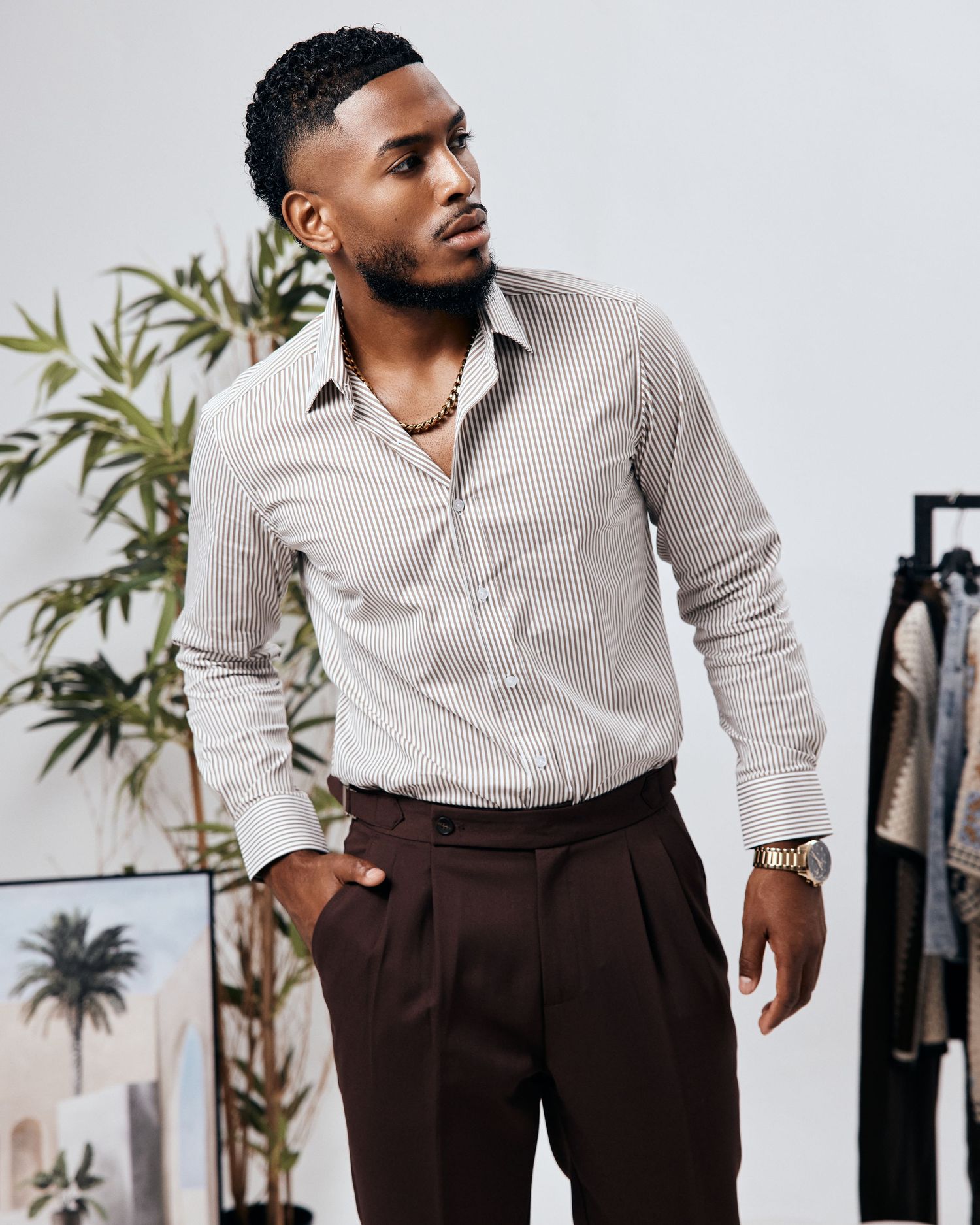 Professional fashion photoshoot of person in striped shirt and dark trousers against studio backdrop.