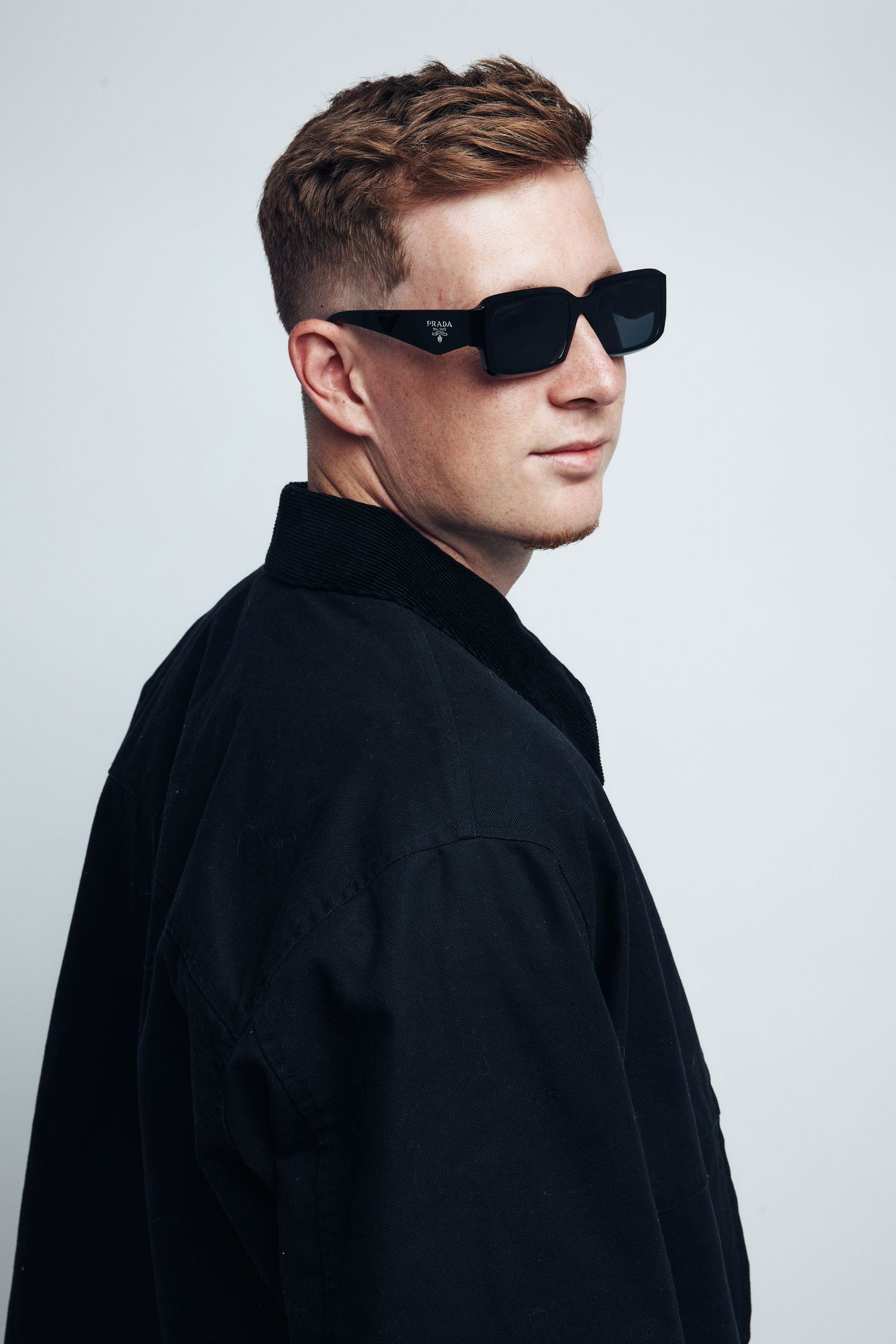 Profile views of person wearing sunglasses and black jacket against white background.