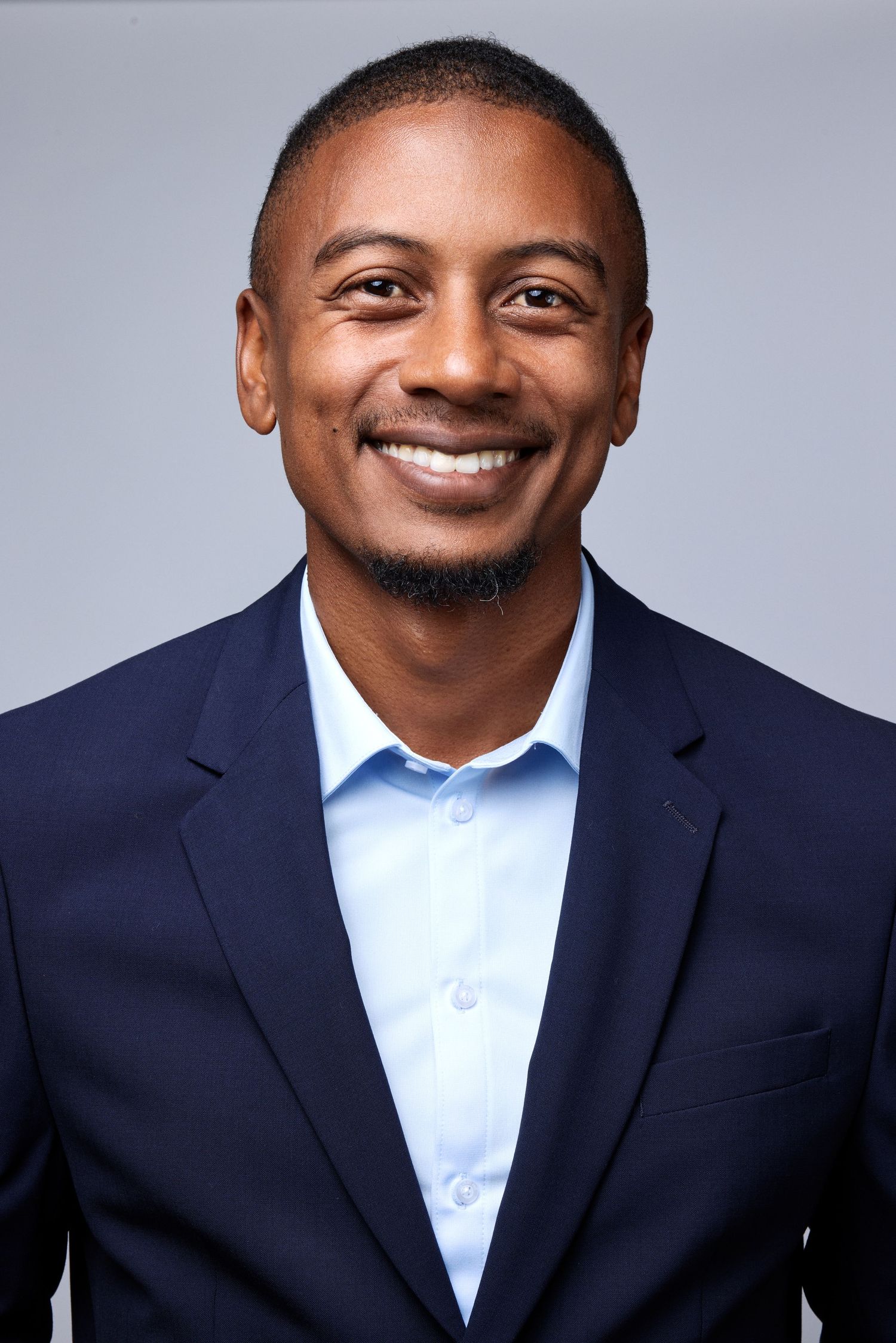Professional wearing navy suit and light blue shirt poses confidently in corporate headshot series.