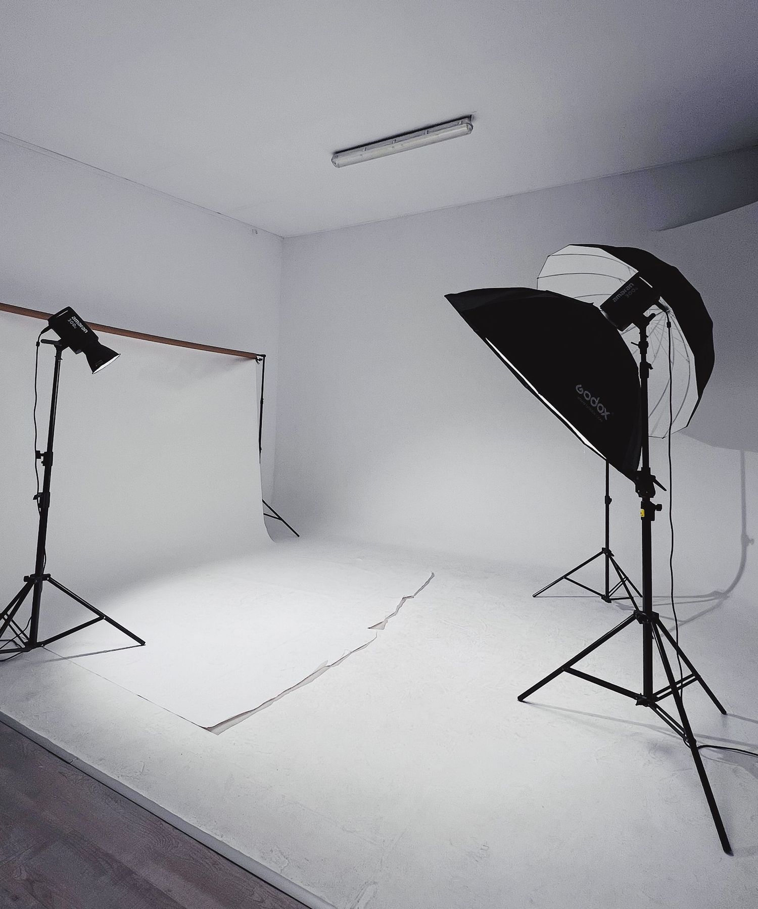Empty white photography studio interior with professional lighting equipment and softboxes set up against seamless backdrop.