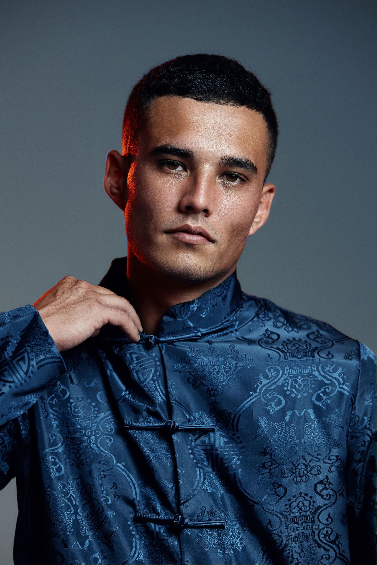 Person wearing blue patterned silk shirt poses dramatically in moody studio portraits.