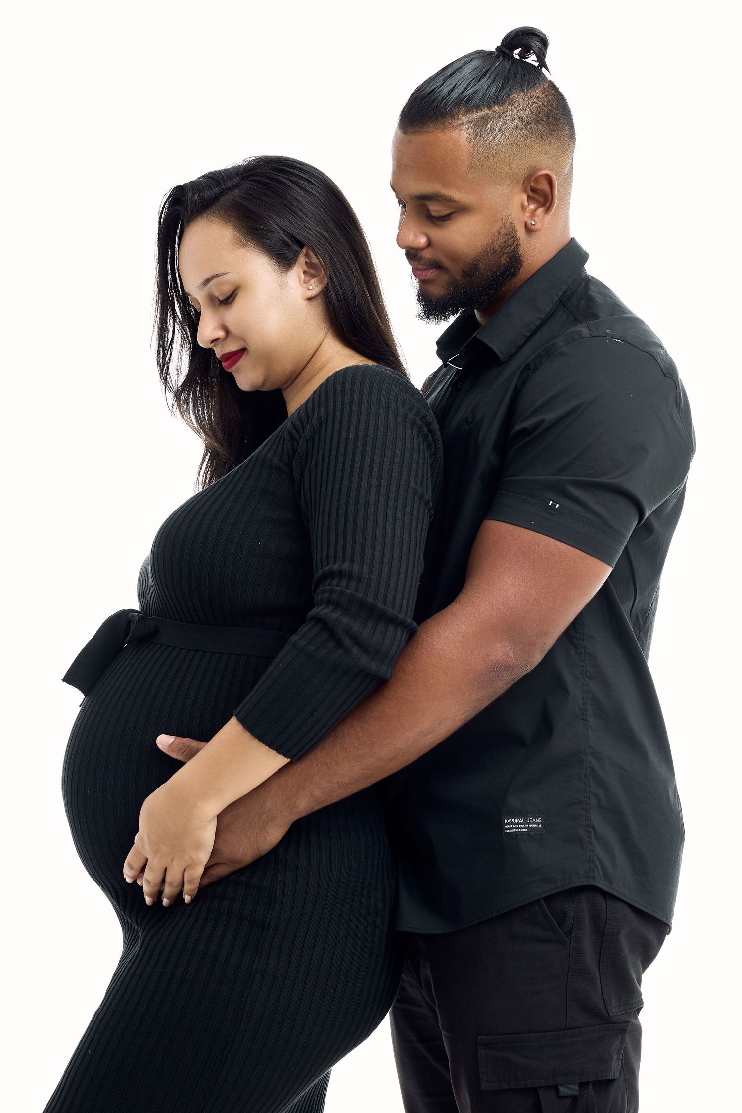 Couple in black outfits embrace lovingly in series of candid studio portraits.