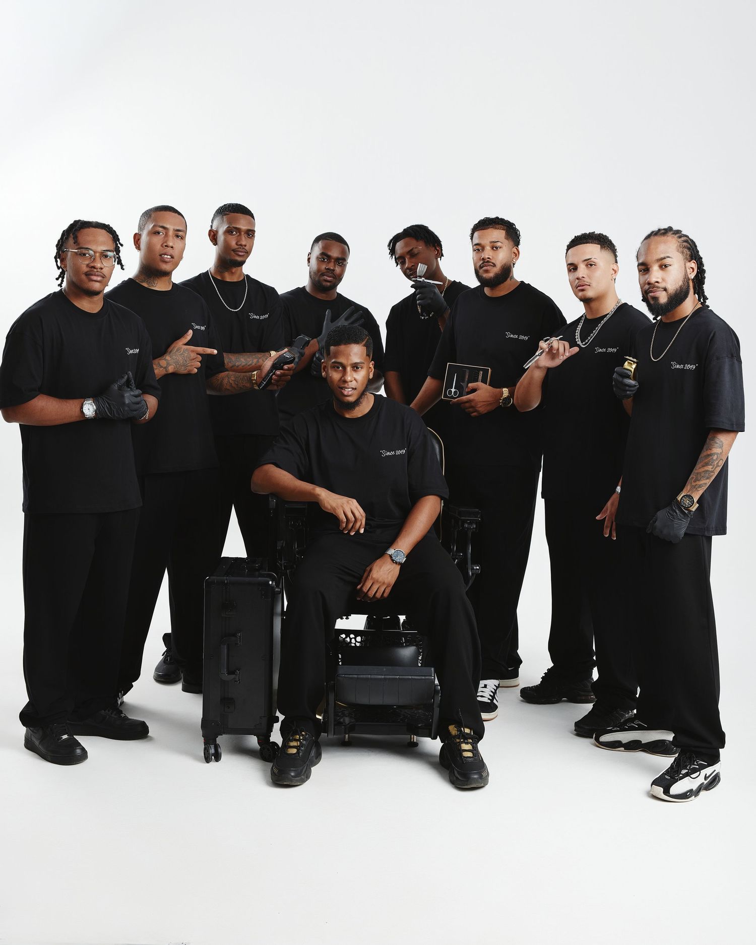 Professional group photo of team members in black attire arranged casually against white backdrop.