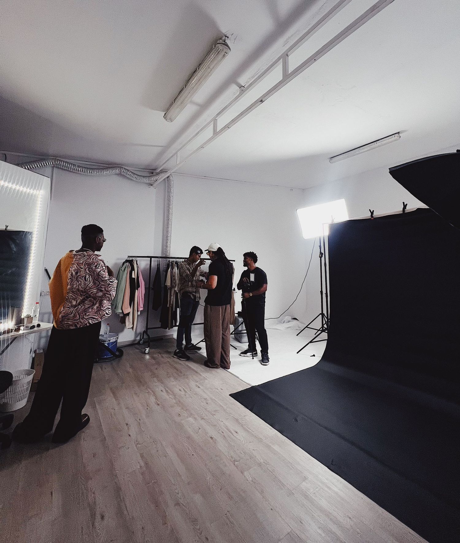 Behind-the-scenes view of a fashion photo shoot setup with clothing racks and lighting equipment in a white studio.