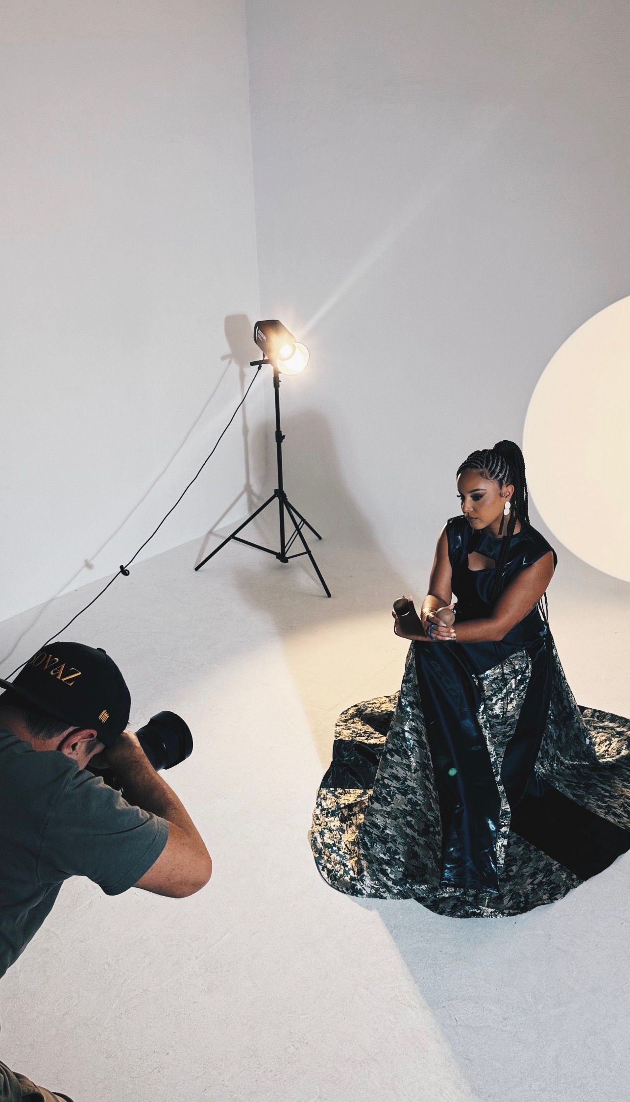 Photographer capturing a woman in an elegant black gown during a professional photo shoot in a white studio with studio lights.