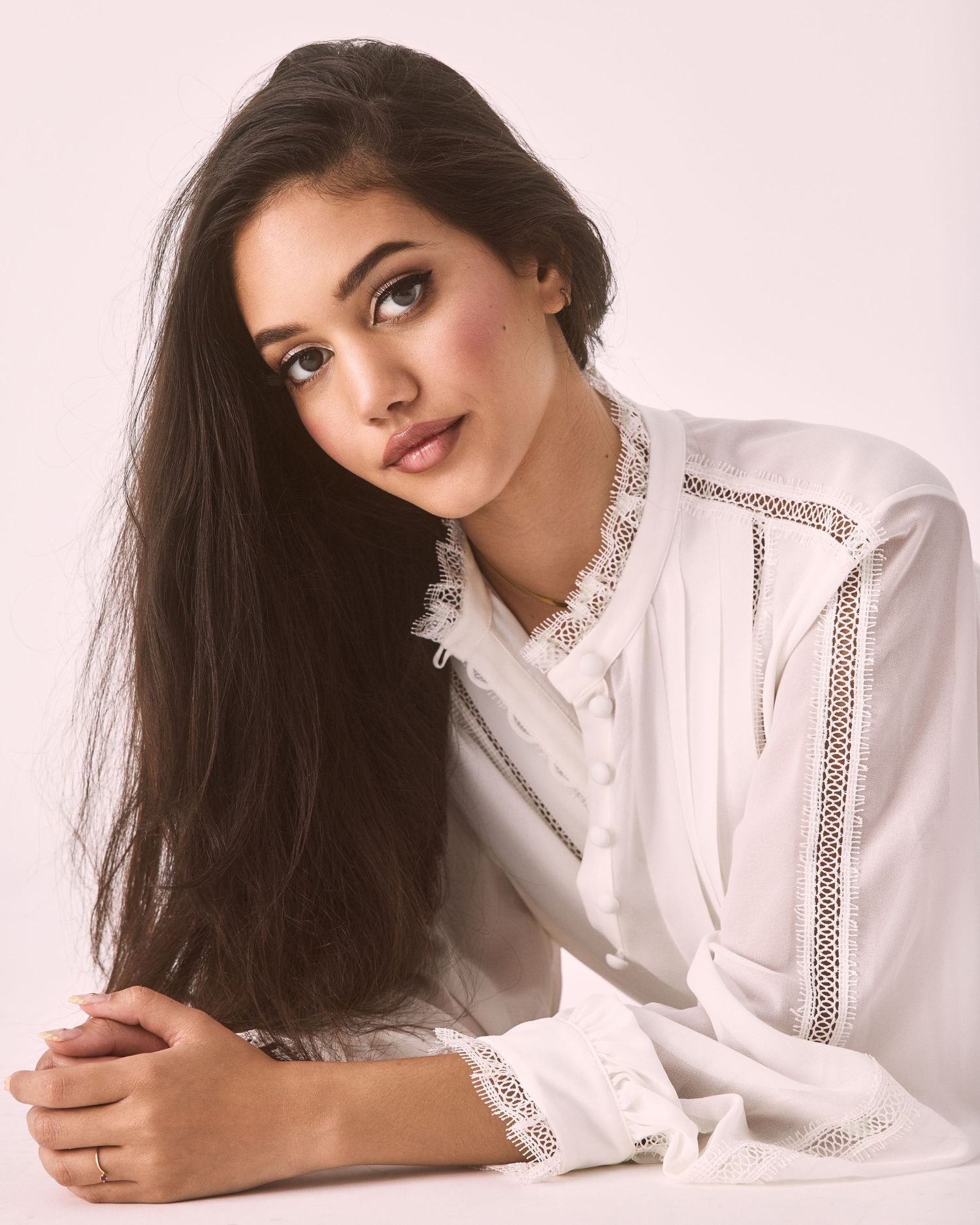 Person in white lace blouse poses gracefully against pink backdrop in fashion portrait series.