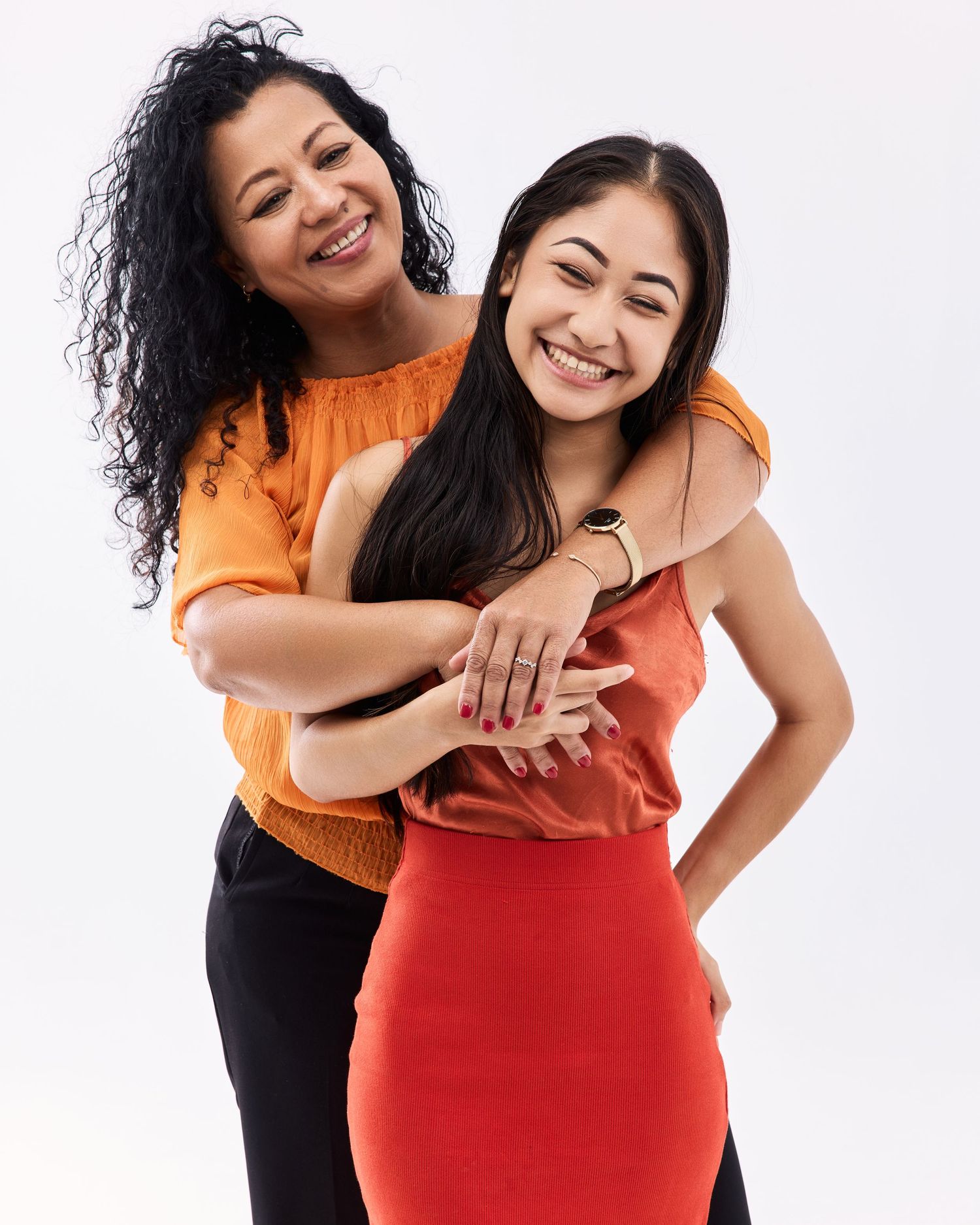 Two people in orange and red outfits embrace and laugh together in a joyful studio photoshoot.