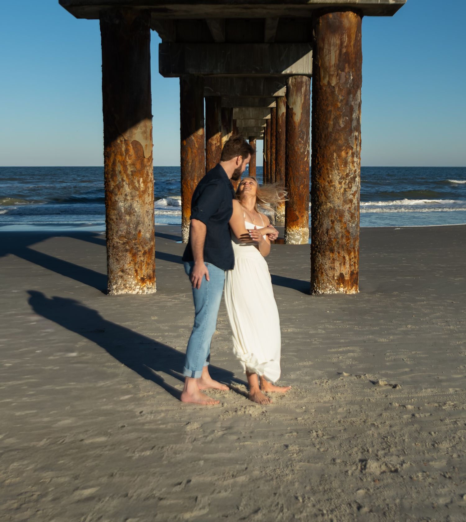 Engagement portraits under the St. Augustine Beach pier, dramatic light by Kaylin Ross Photography