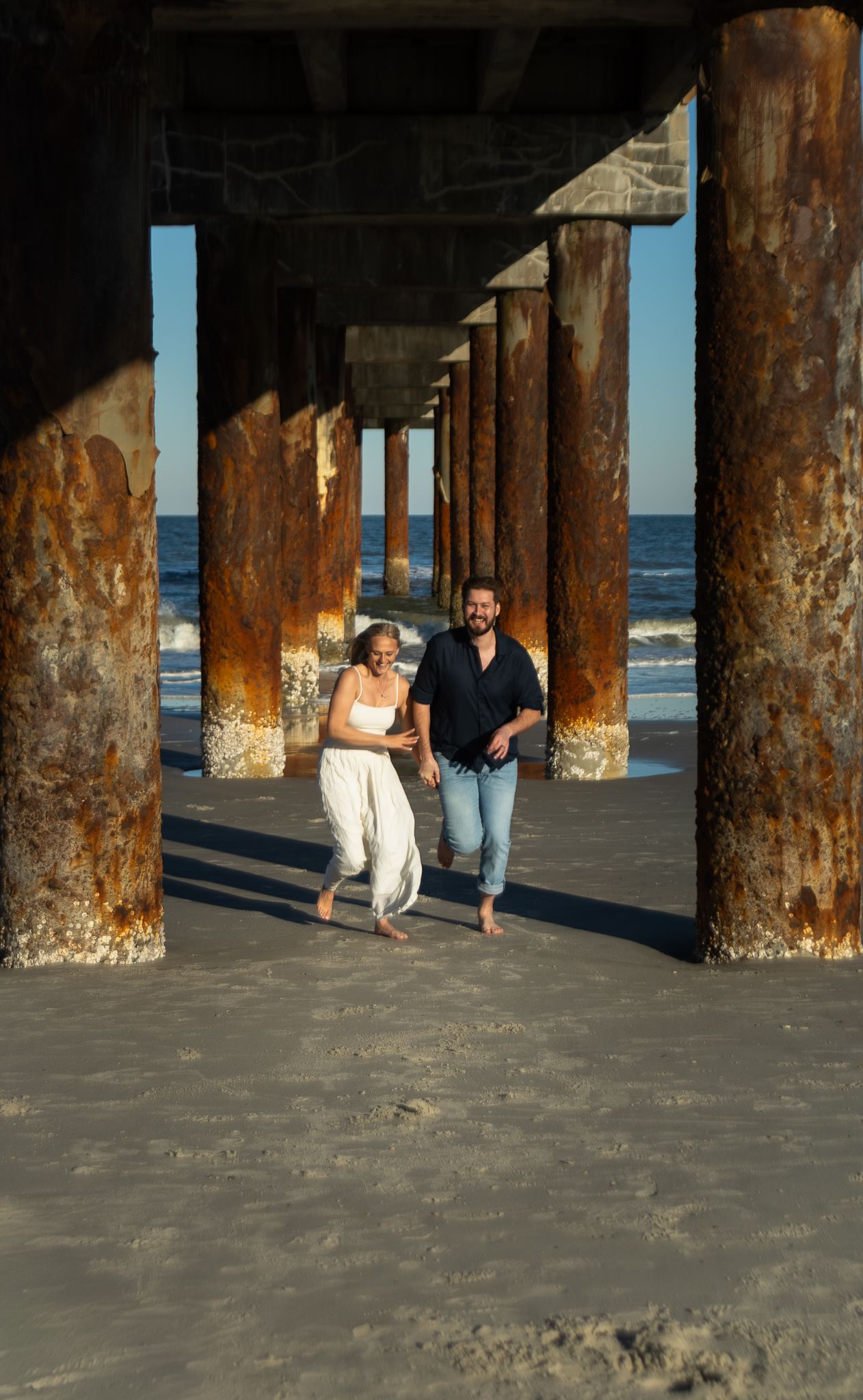 Engagement portraits under the St. Augustine Beach pier, dramatic light by Kaylin Ross Photography