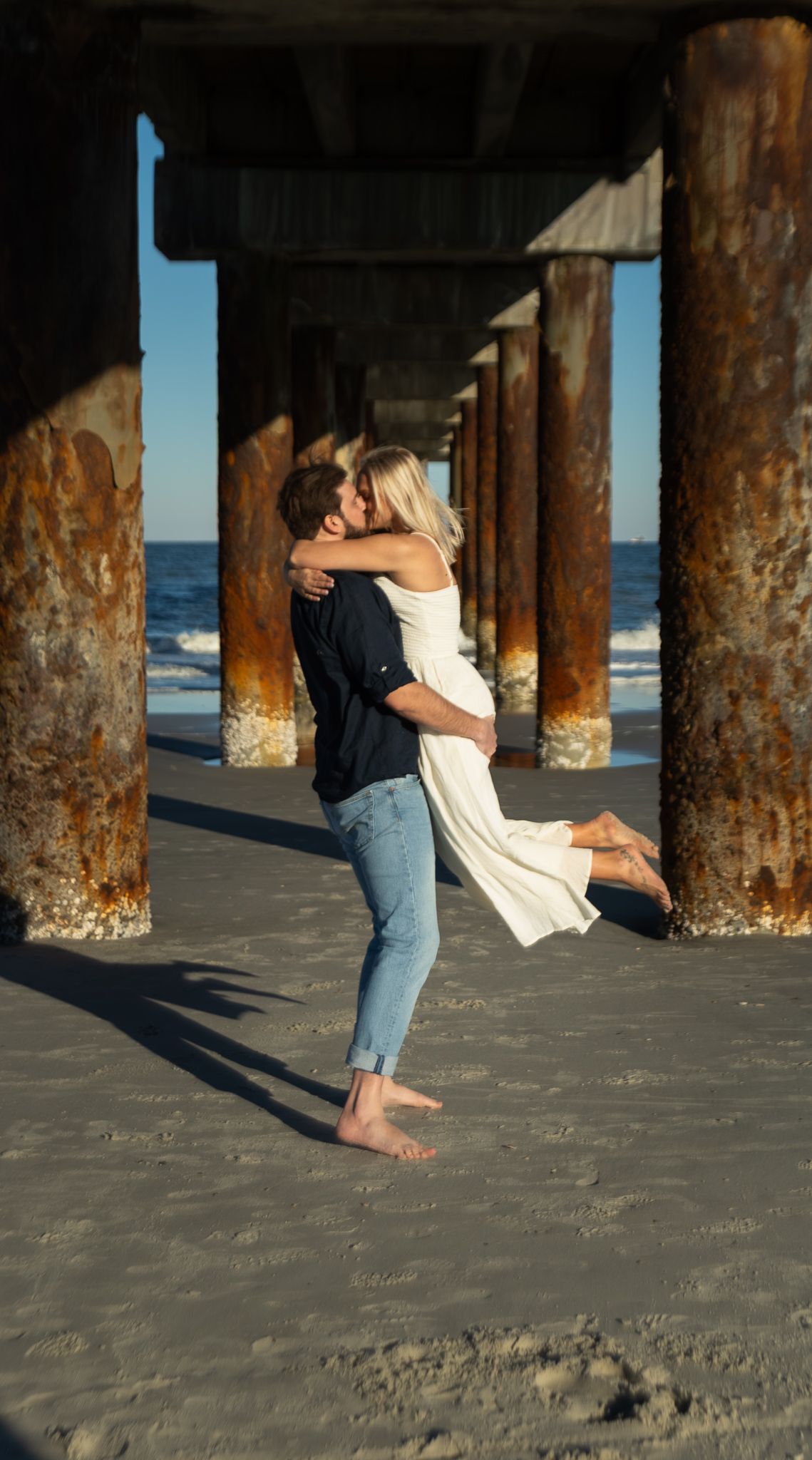 Engagement portraits under the St. Augustine Beach pier, dramatic light by Kaylin Ross Photography