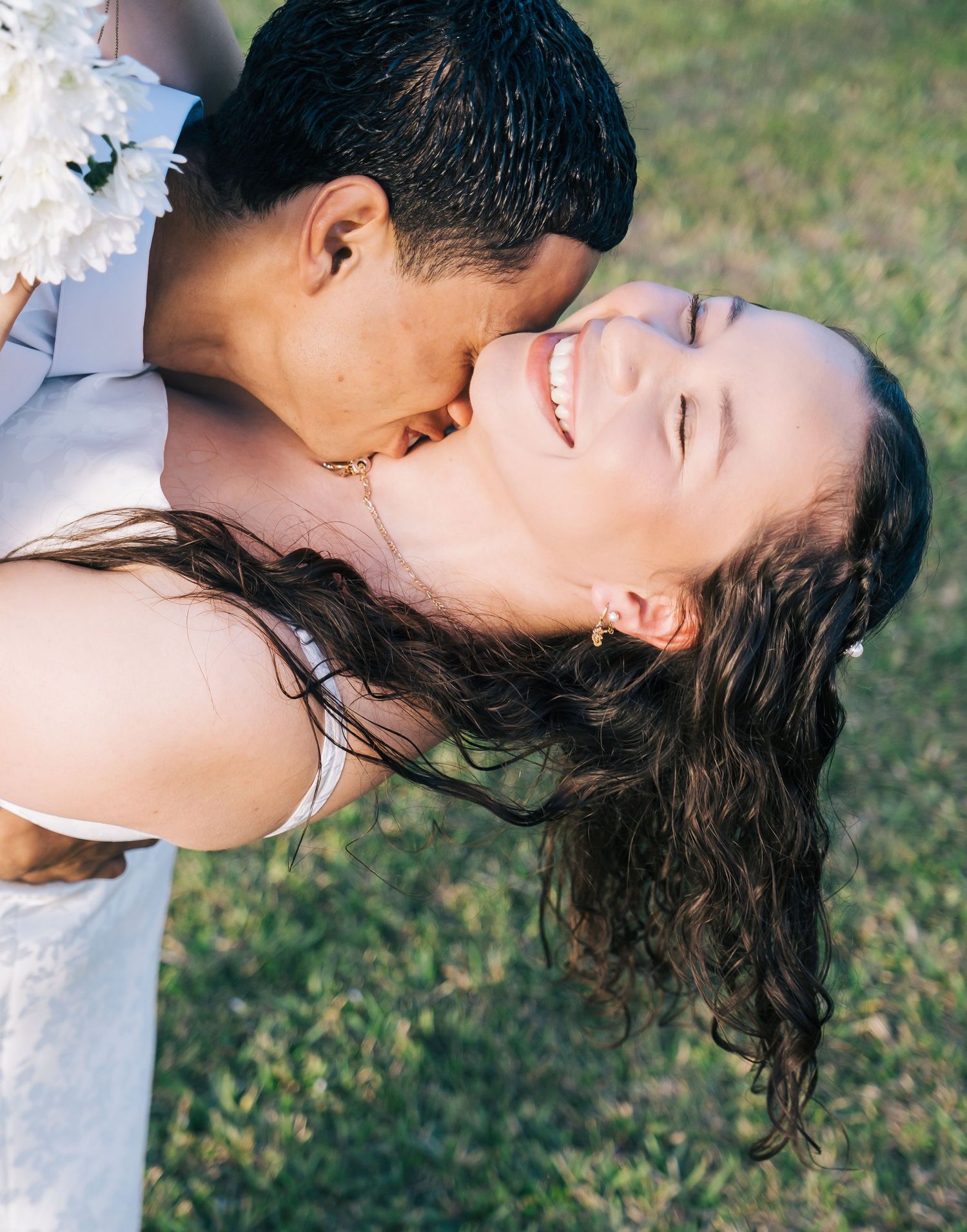 A romantic couple embracing on grass during a sunny outdoor photoshoot.