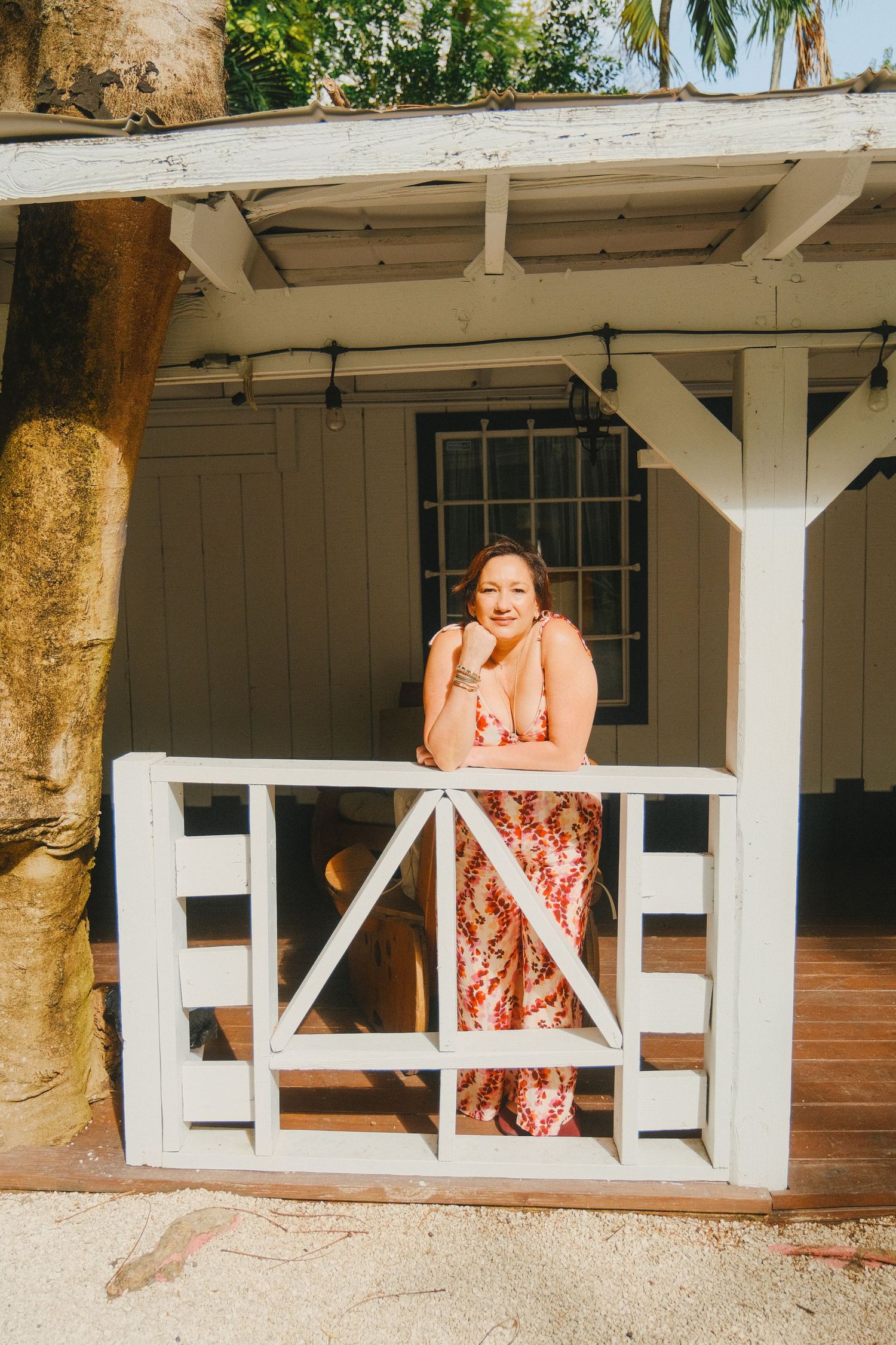 Three connected photos show someone in a floral dress sitting and posing on a white porch railing at different angles.