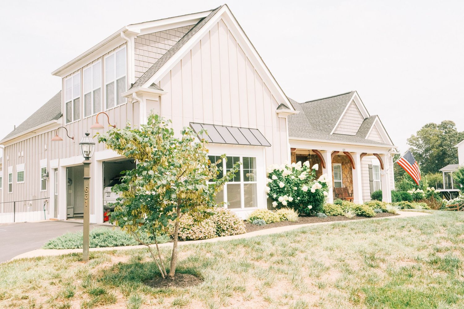 Modern farmhouse wedding venue with white board-and-batten siding, metal roof, and lush landscaping on a sunny day.