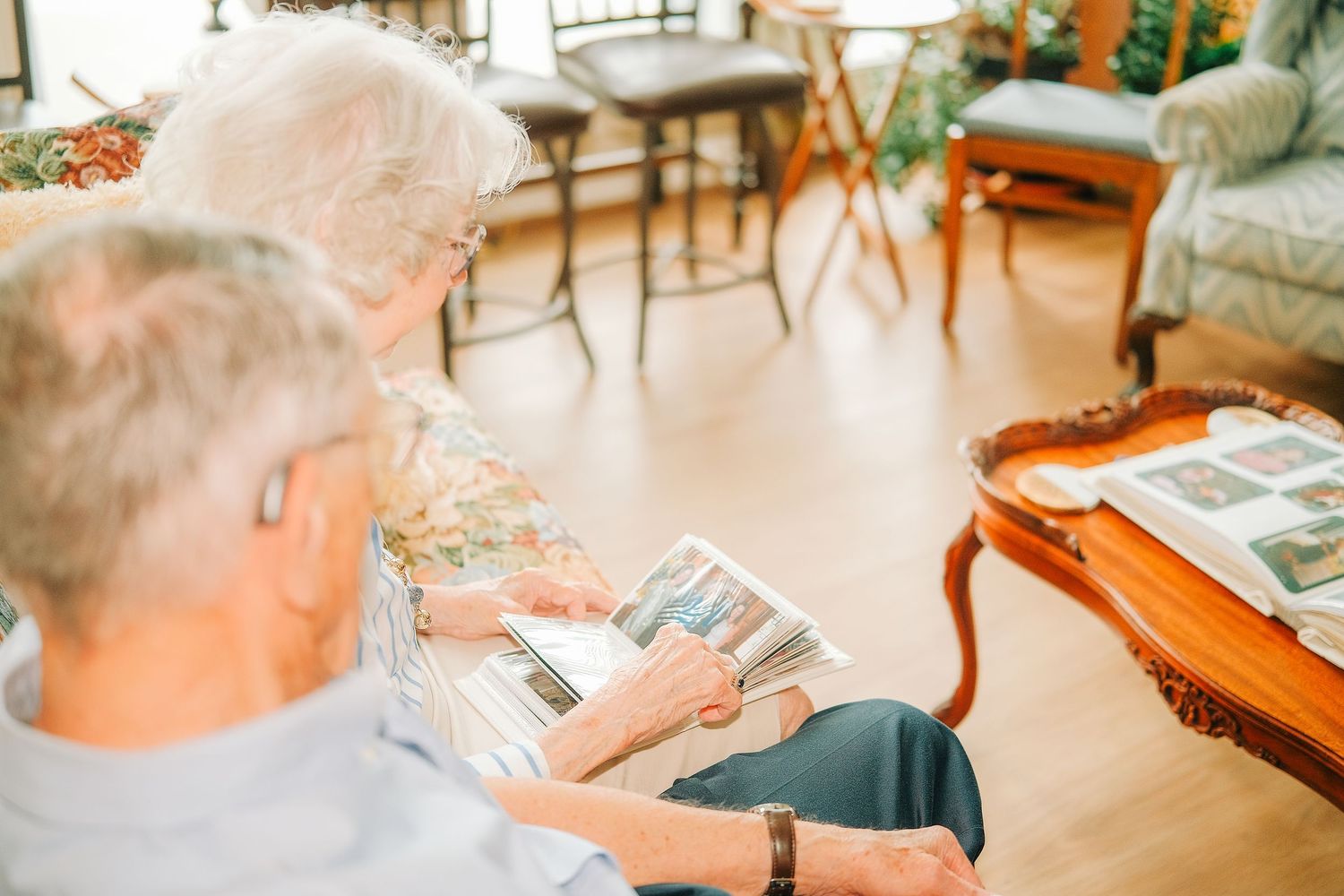 Two elderly people sit together reviewing a photo album in a cozy, well-lit living room.