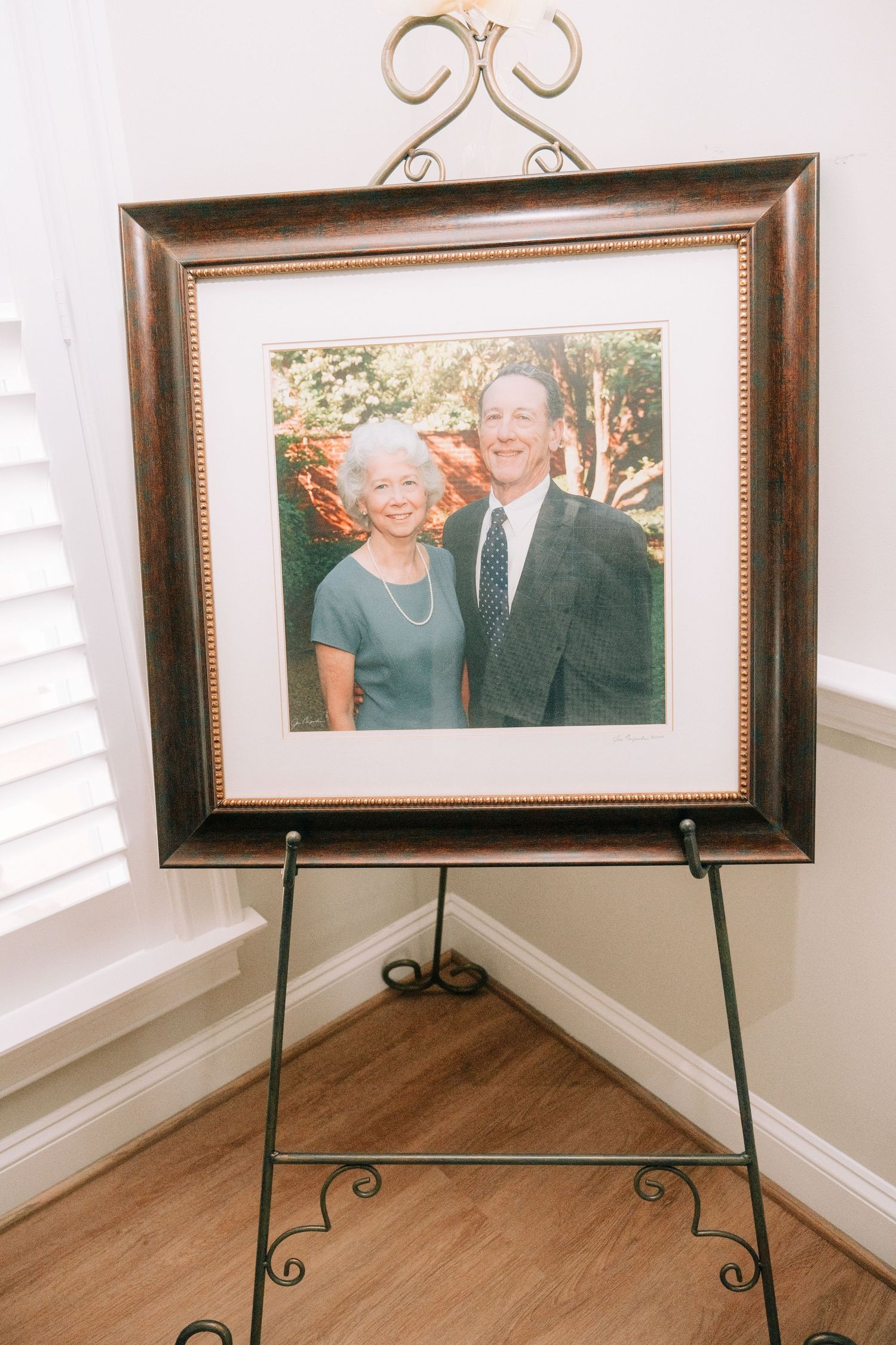 Framed portrait of a smiling older couple displayed on an easel in a bright room.