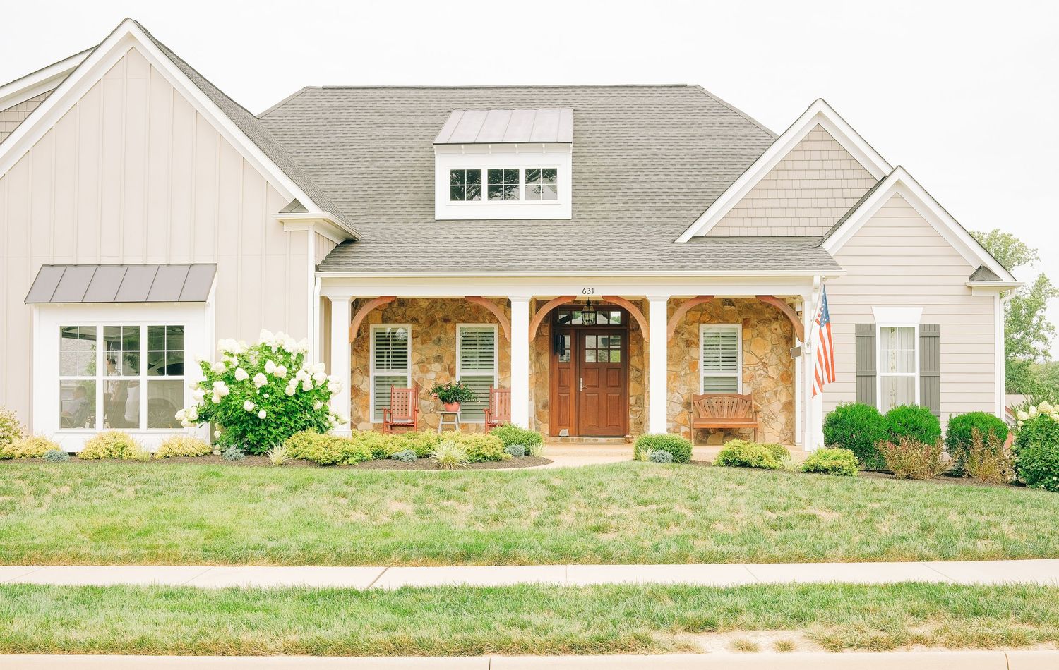 Charming craftsman-style home with stone accents, covered porch, and American flag on a well-manicured lawn.