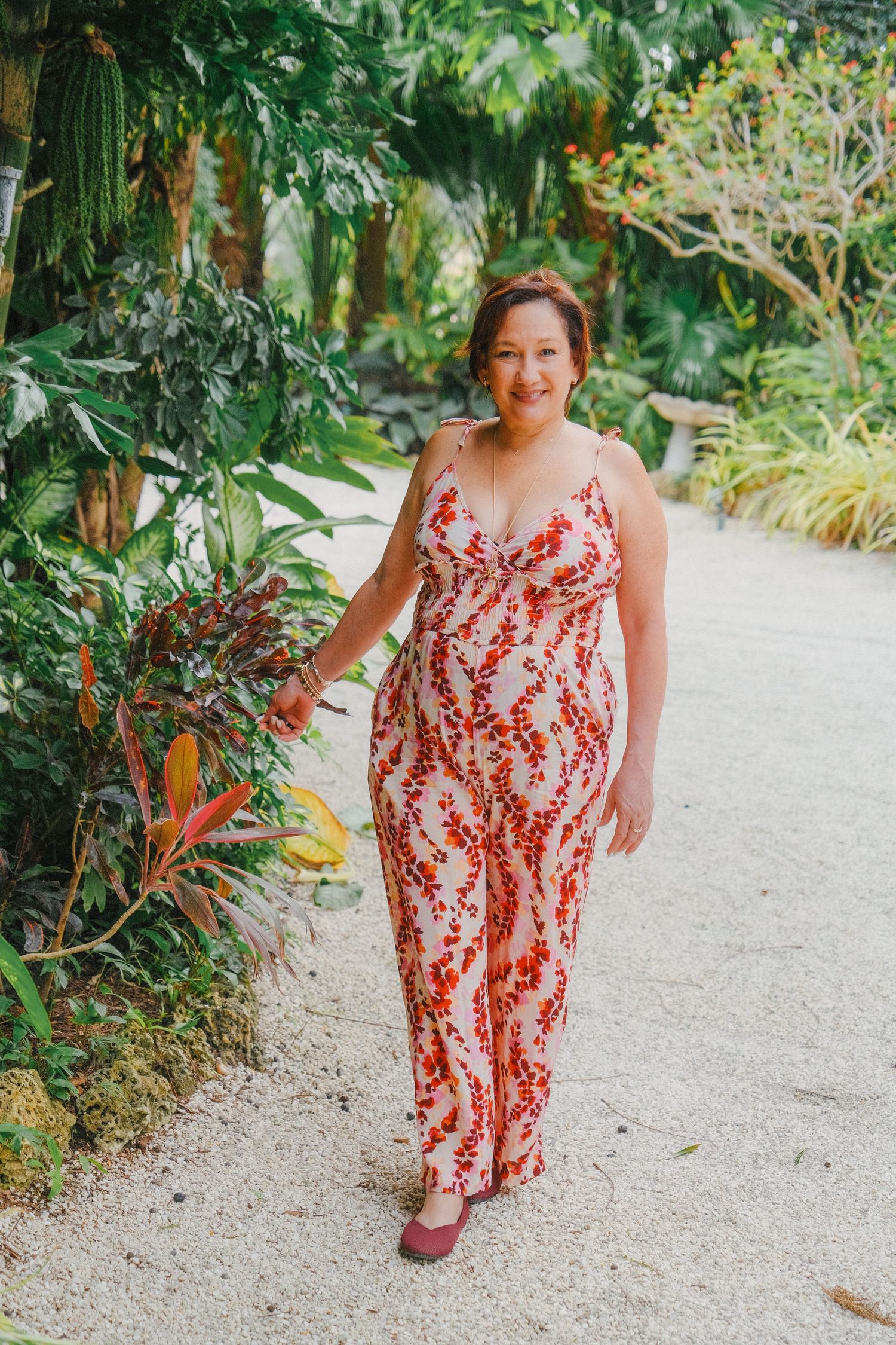 Someone wearing a red and white patterned maxi dress walks along a garden path surrounded by tropical plants.