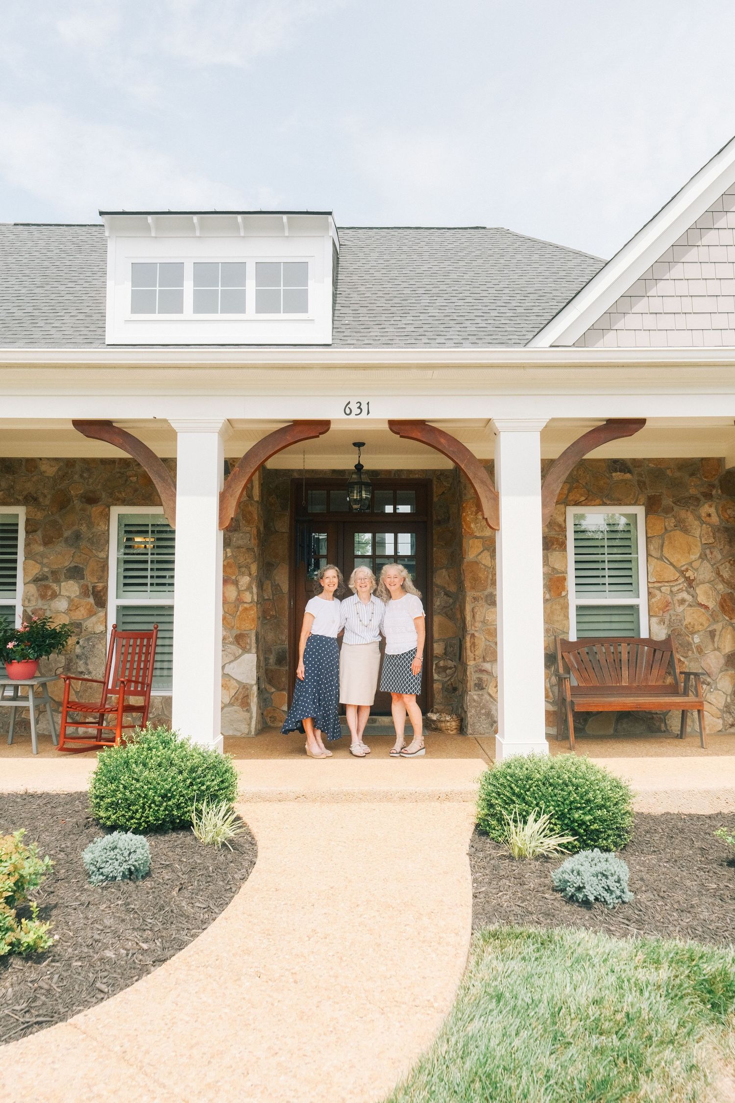 Three women pose together on the covered front porch of a charming stone house.