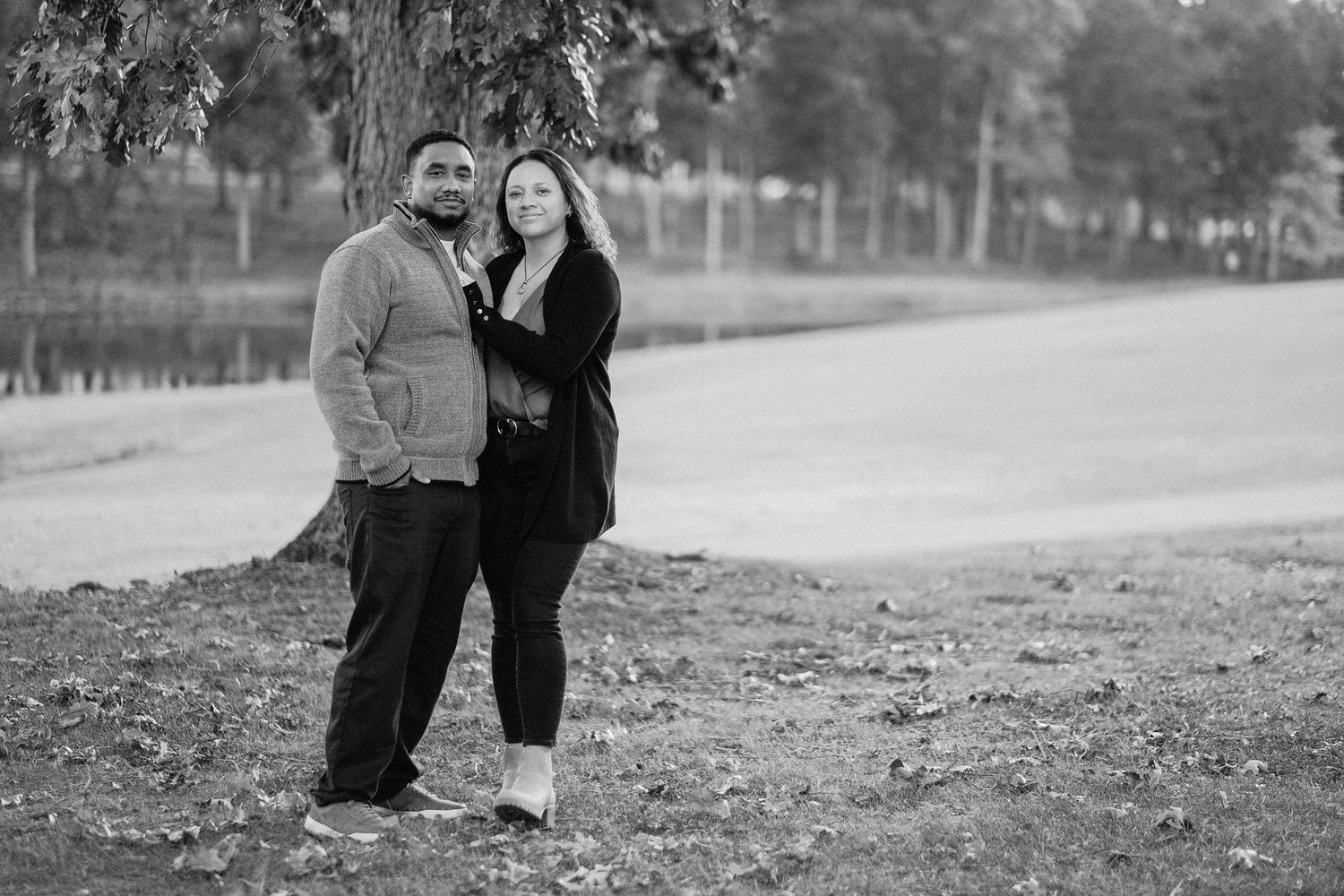 A couple shares an intimate moment outdoors during a black and white photo session in a park setting.