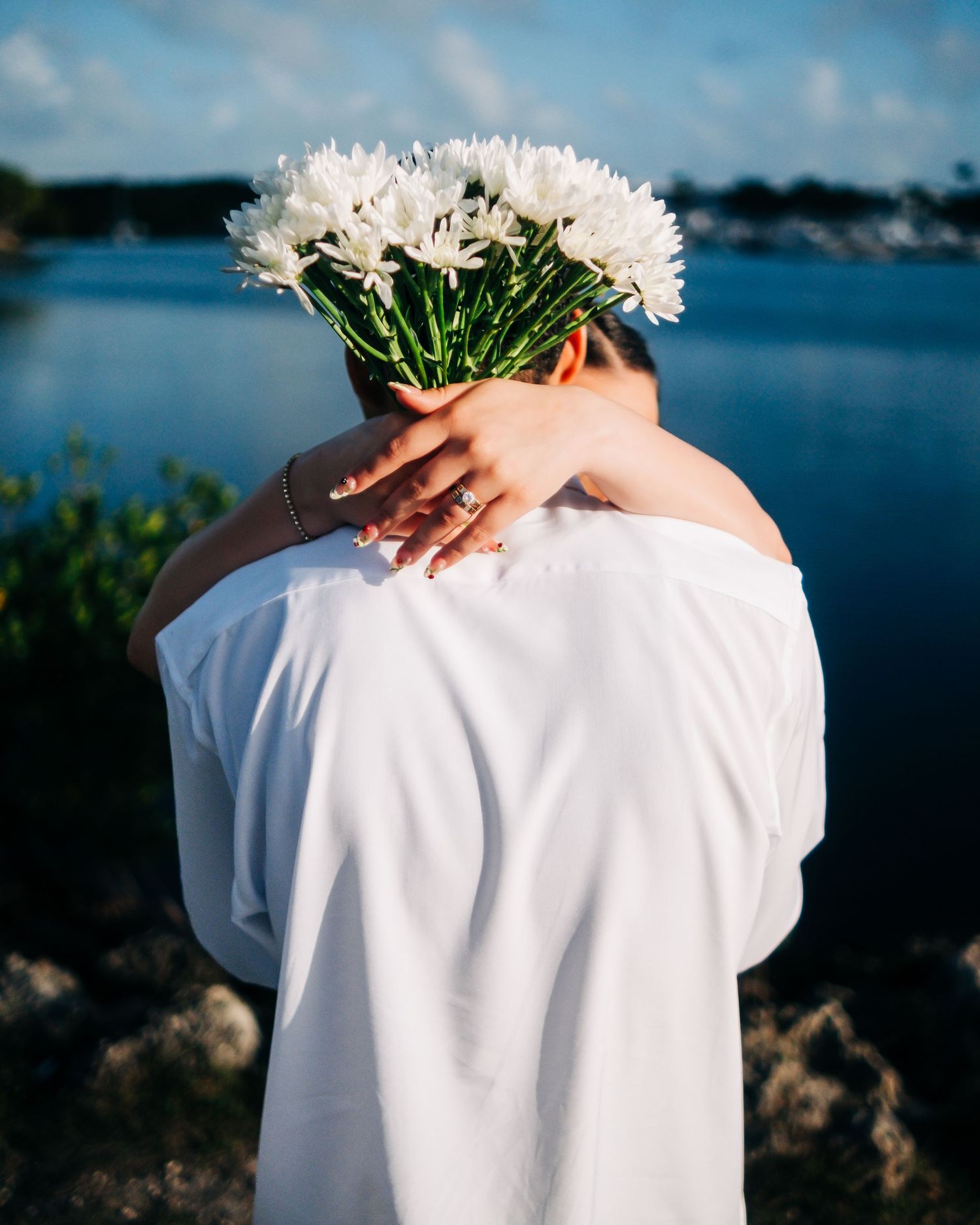 White daisies held against a white shirt with ocean and blue sky in the background.