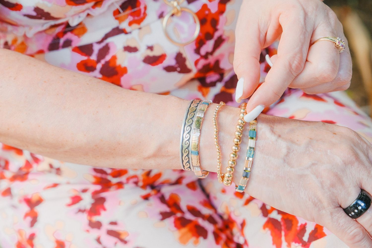 Hands wearing multiple colorful rings against a floral patterned background.