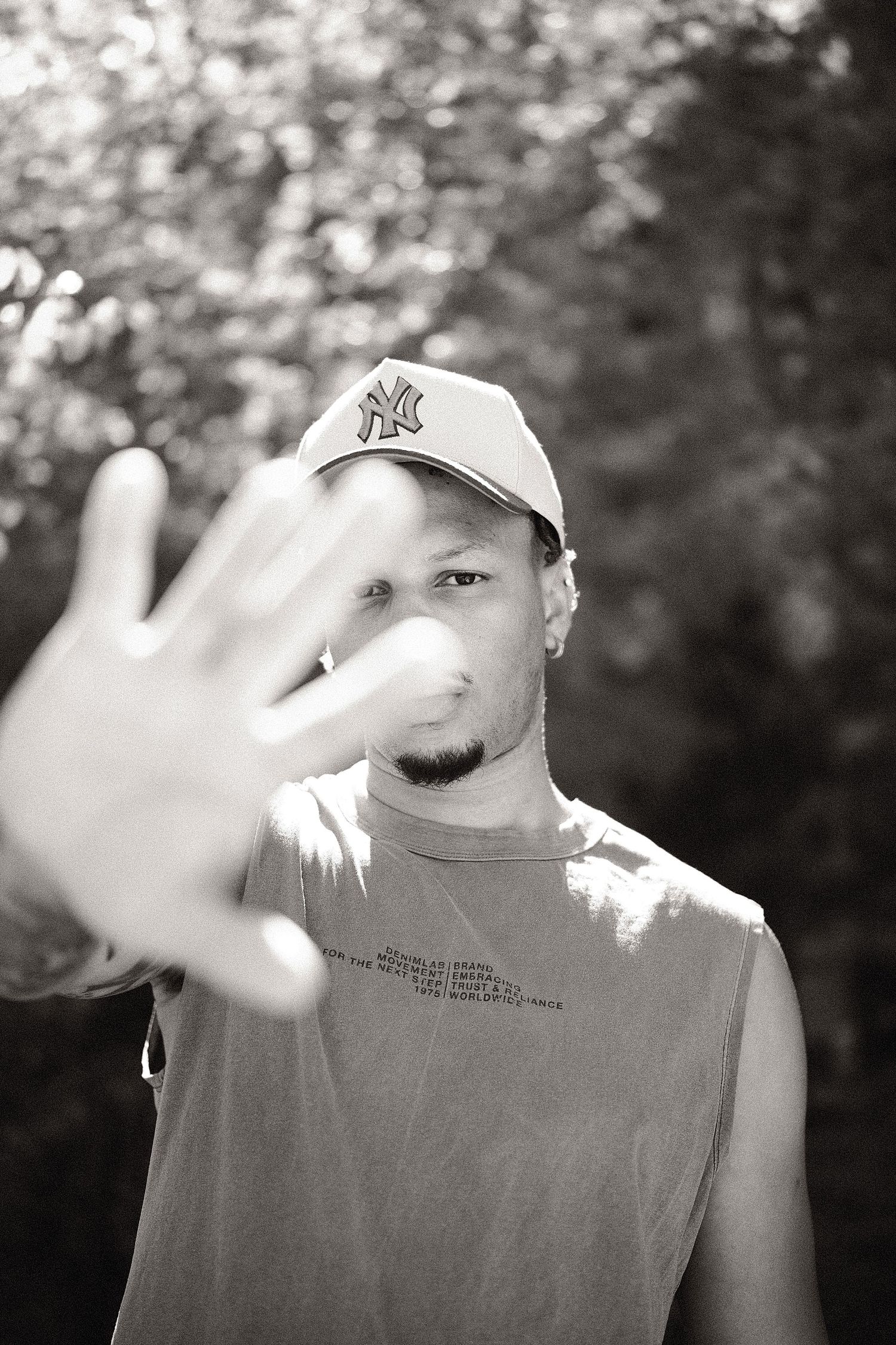 Black and white photo of a young man in NY Yankees cap extending hand toward camera outdoors.