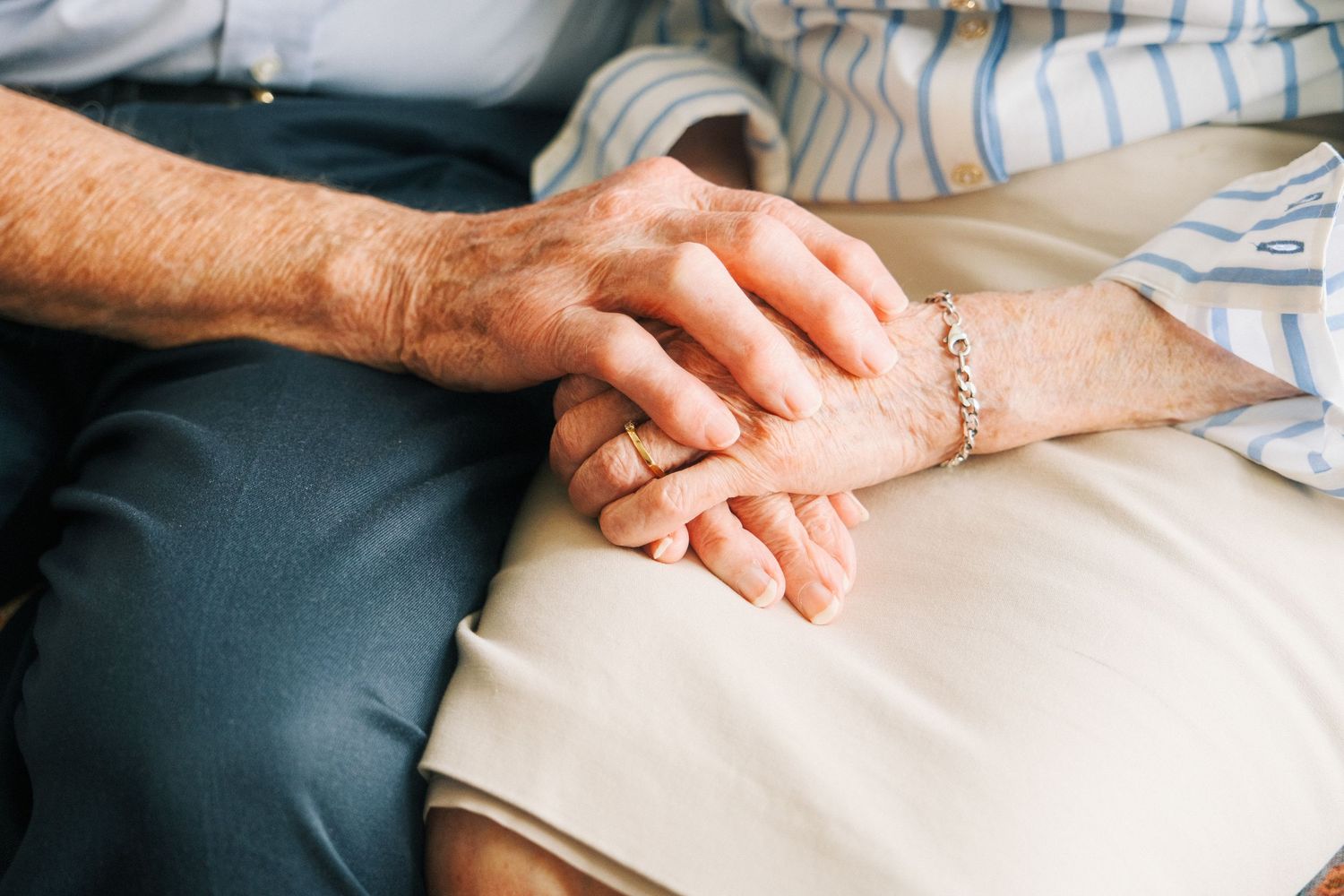 Two elderly people holding hands tenderly, showing love and companionship in their golden years.