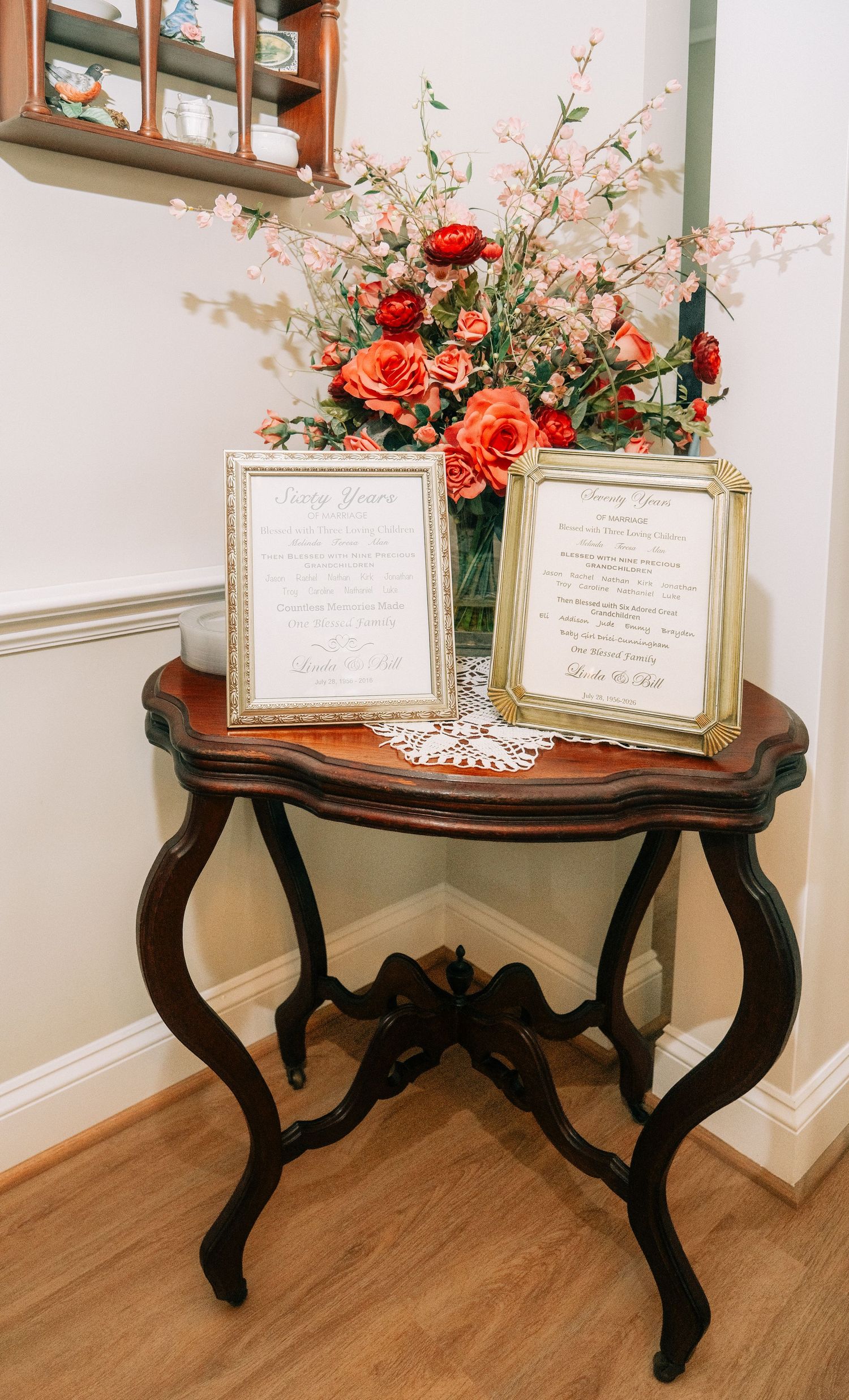 Elegant antique side table with framed wedding vows, orange roses bouquet, and decorative doily in a home setting.