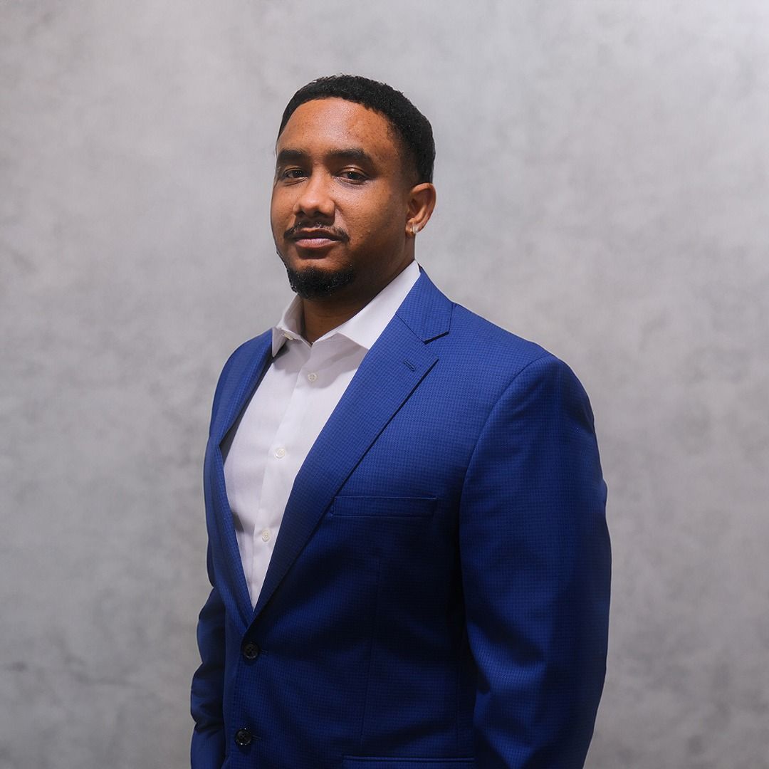 Professional headshot of someone in a royal blue suit jacket and white dress shirt against a gray background.