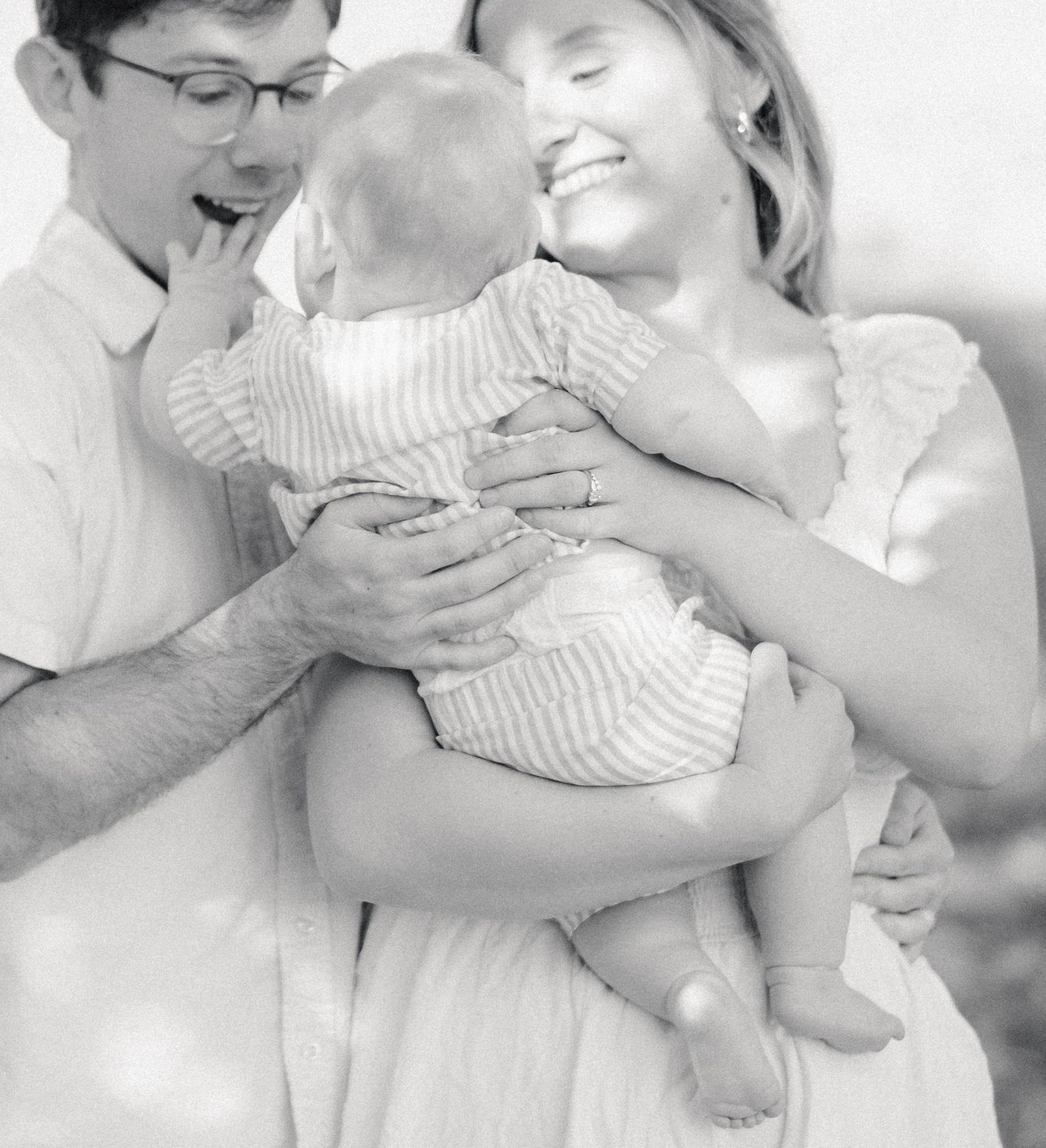 Black and white photo of happy parents smiling and holding their newborn baby together outdoors.