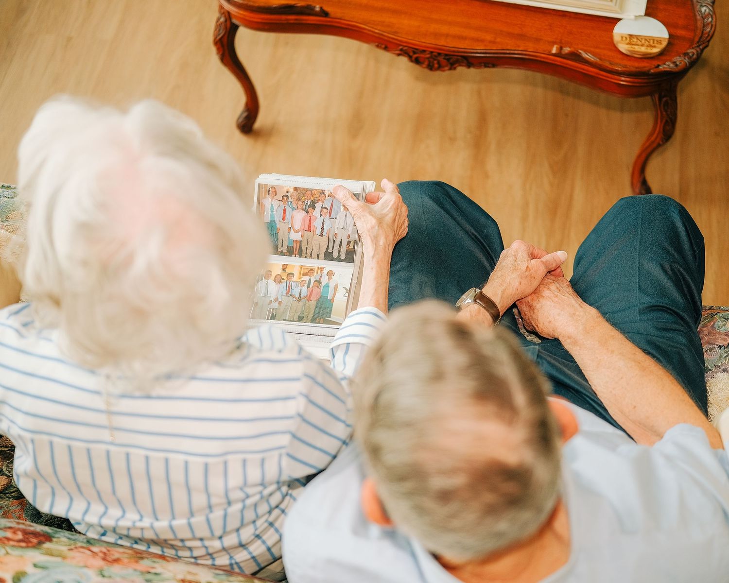 Elderly couple sitting together on floor looking at photo album, viewed from above in cozy living room.