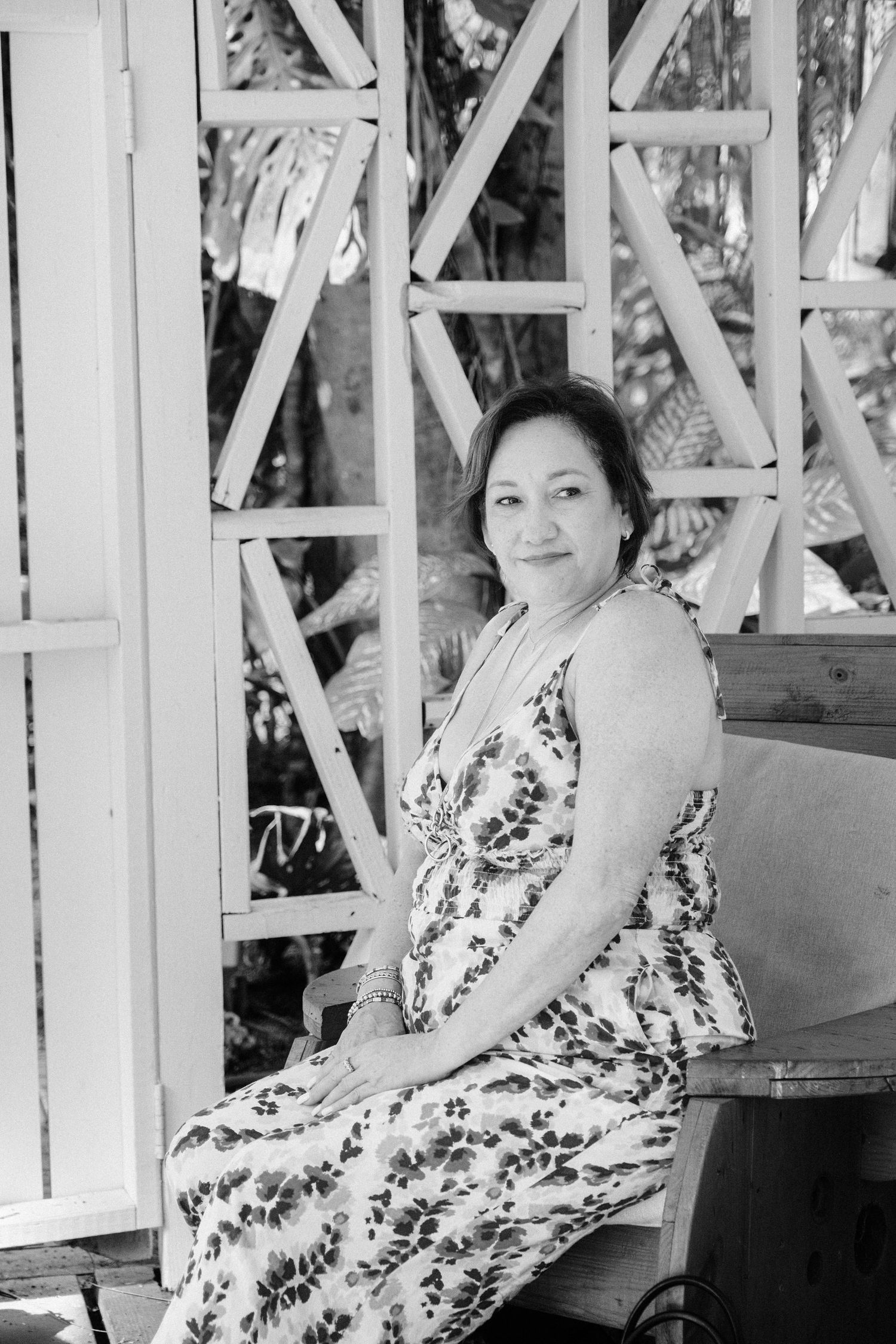 A person in a floral dress sits on a bench in a black and white vintage photograph.