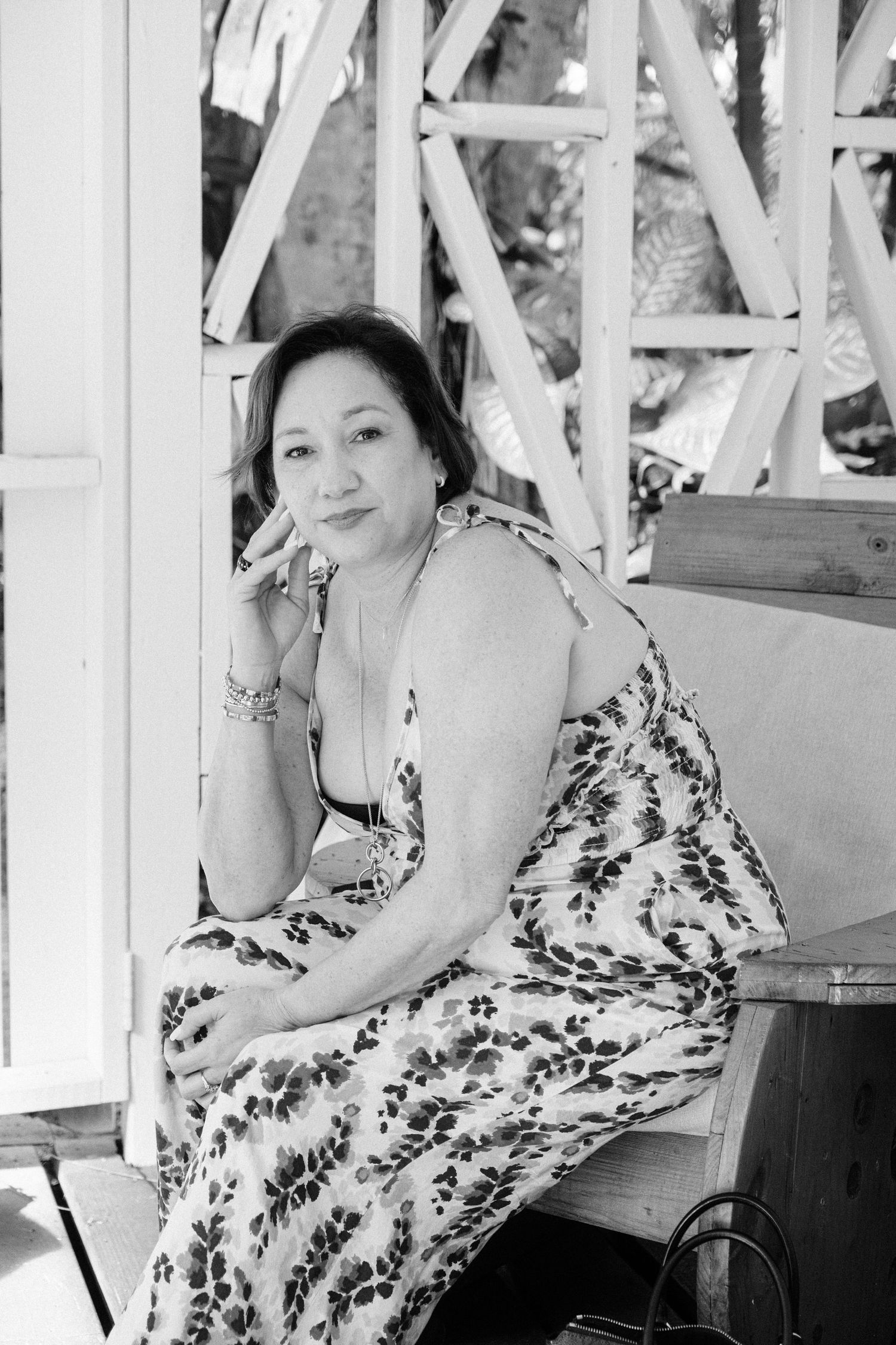 Black and white portrait of someone in a floral print sundress sitting on wooden steps outdoors.