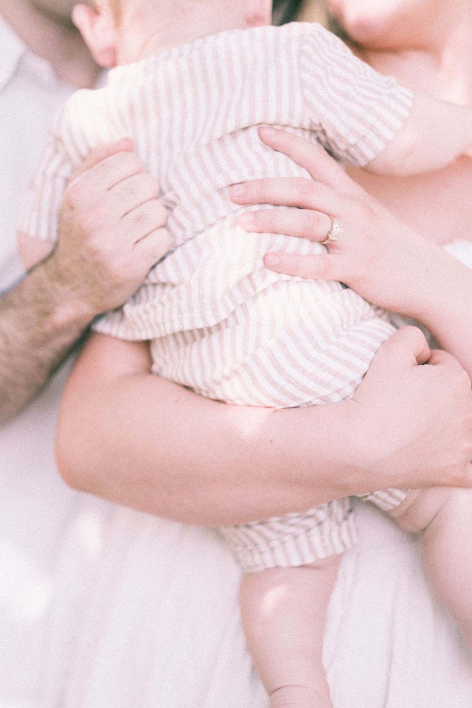 Parents holding a newborn baby dressed in a pink striped romper, close-up family photo.