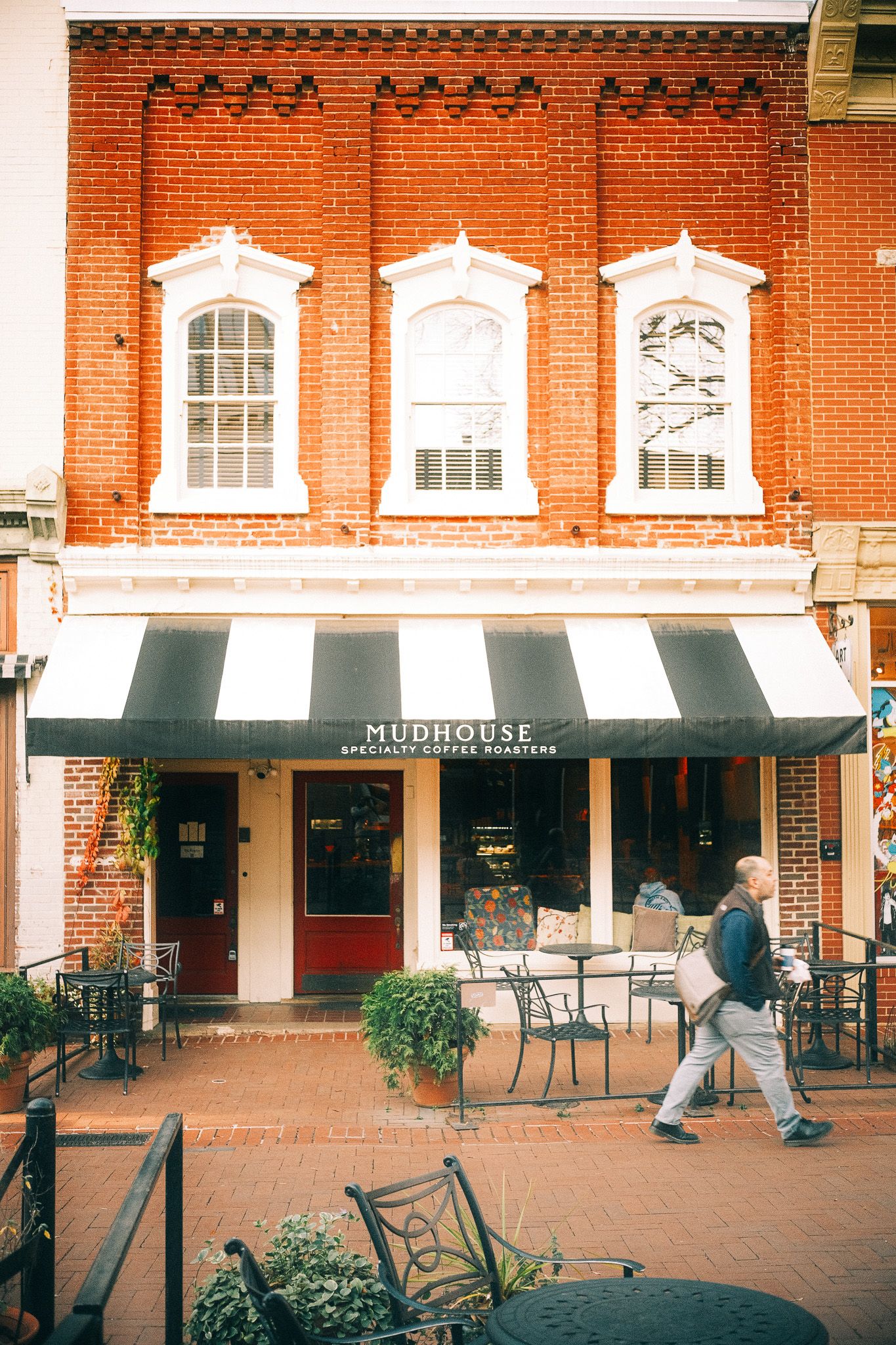 Historic brick building with white-trimmed windows and striped awning above Mudhouse storefront.